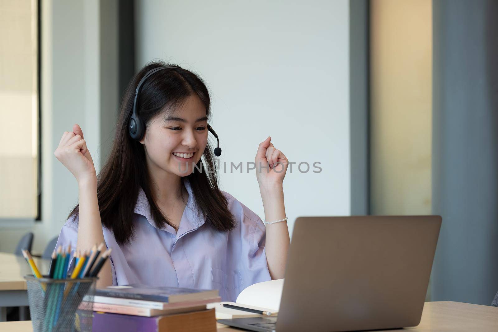 Cheerful asian girl wear wireless headset laughing with laptop - online education concept