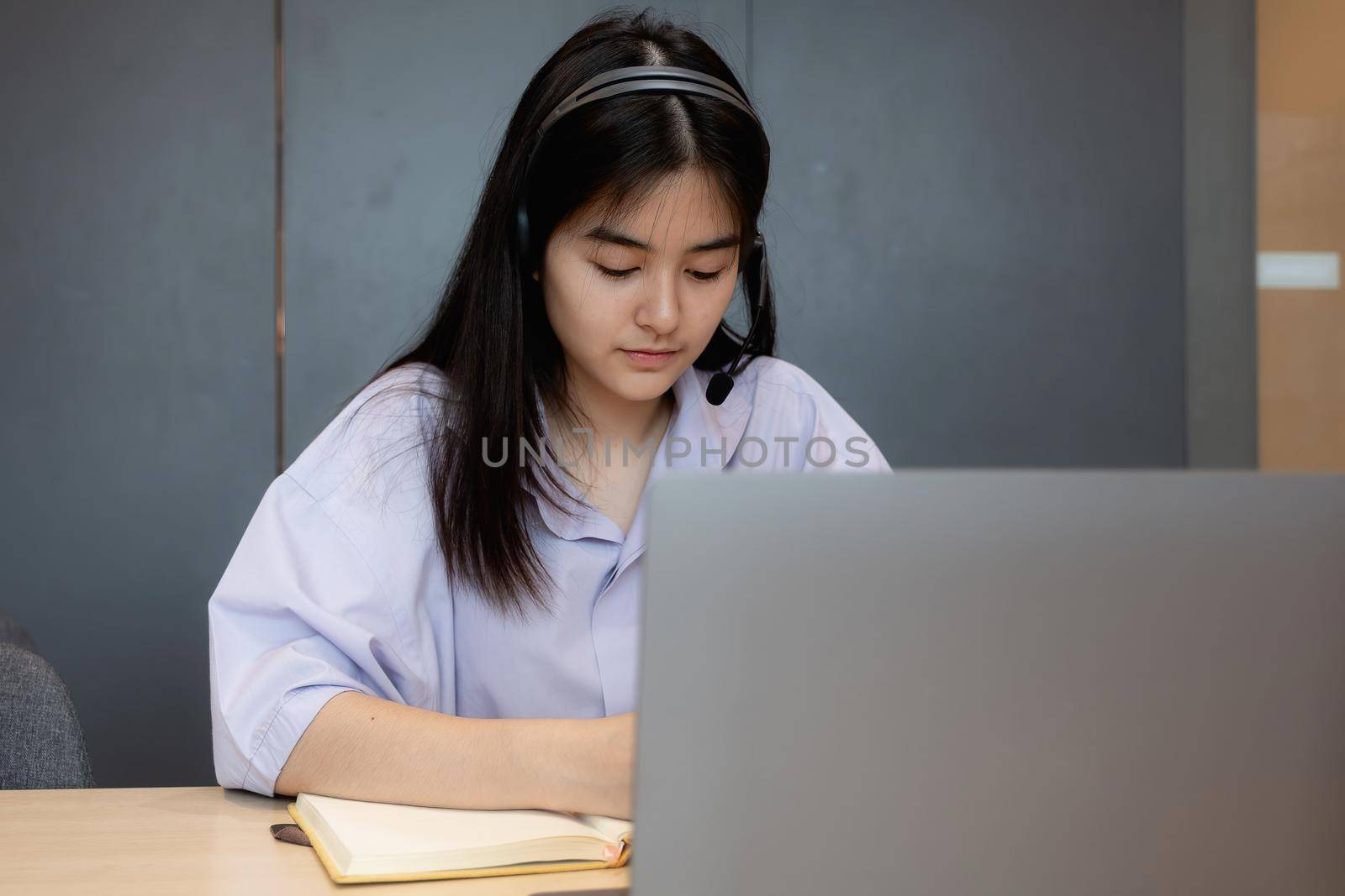 Asian student making notes during online lesson with laptop at home.