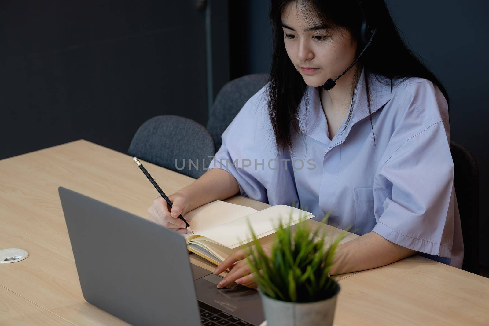 Asian student making notes during online lesson with laptop at home.