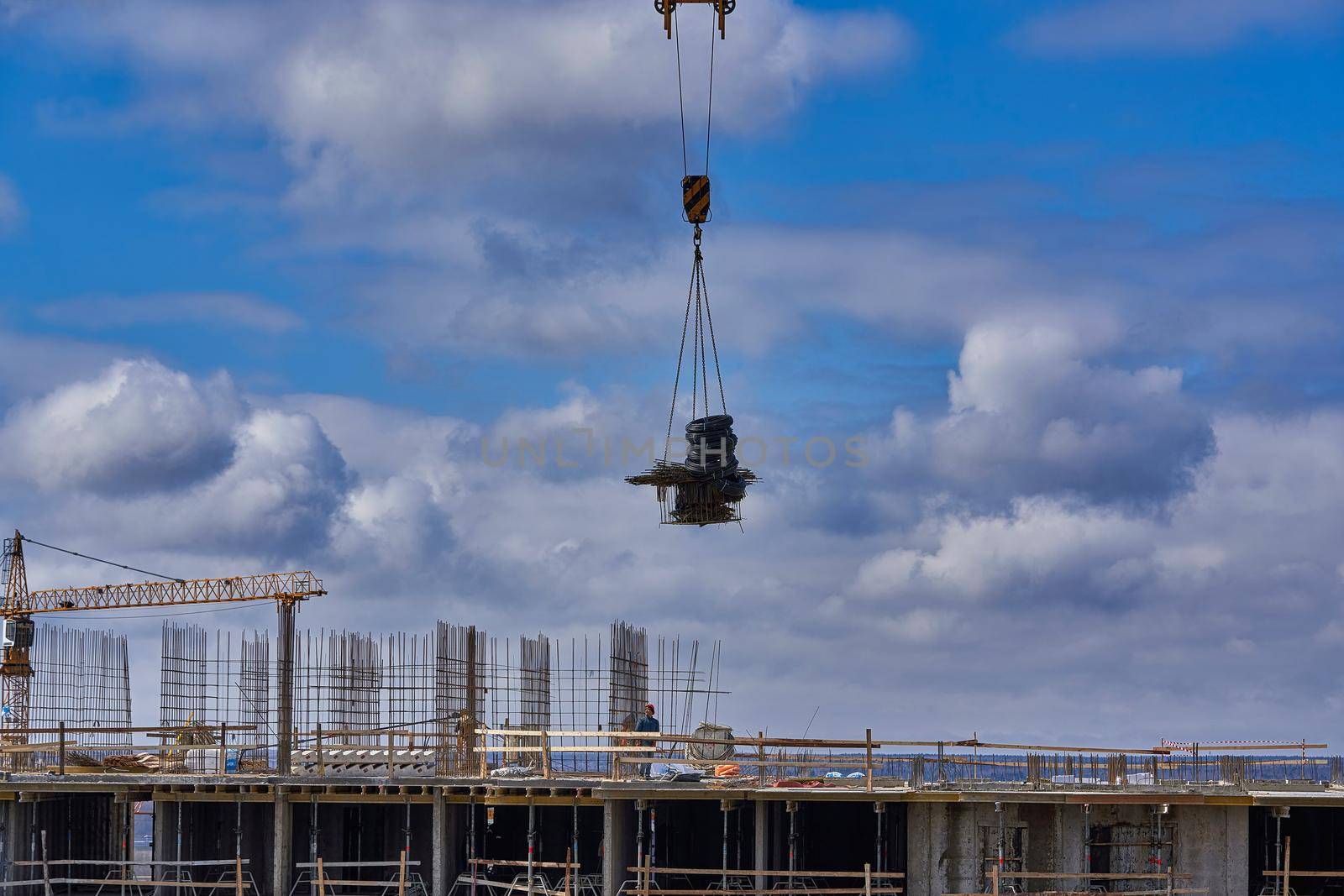 load is suspended from the cable of a crane against background of a cloudy sky by vizland