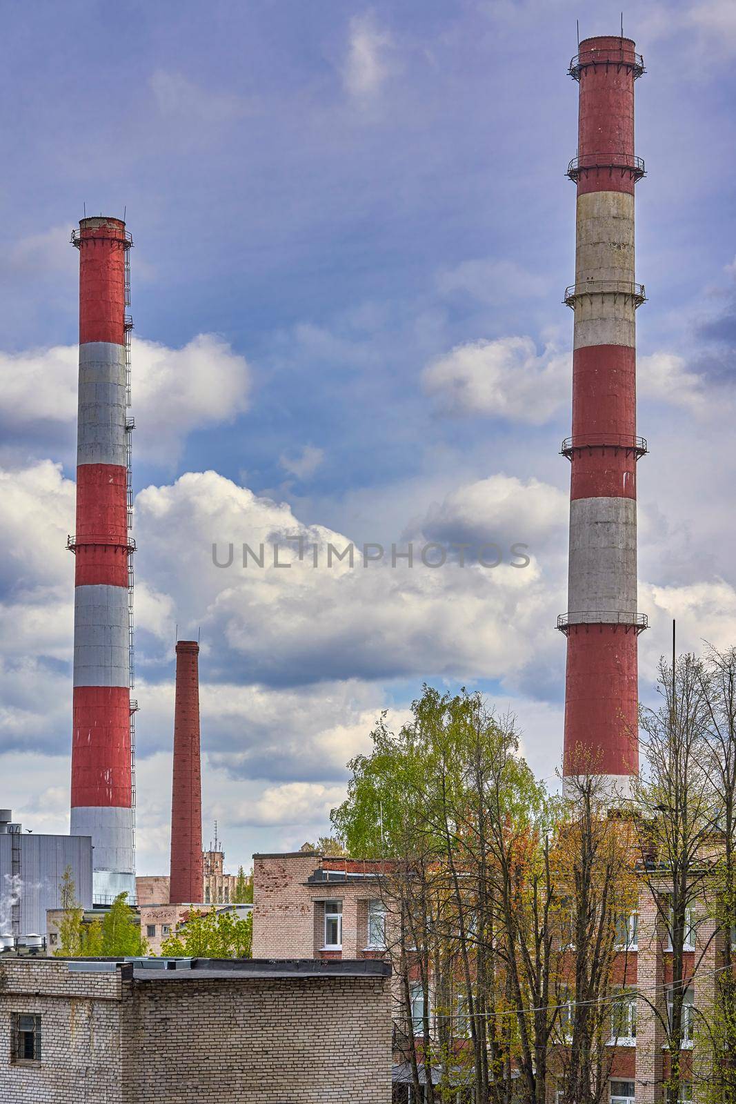 Tall factory chimneys against backdrop of a cloudy sky and residential buildings by vizland