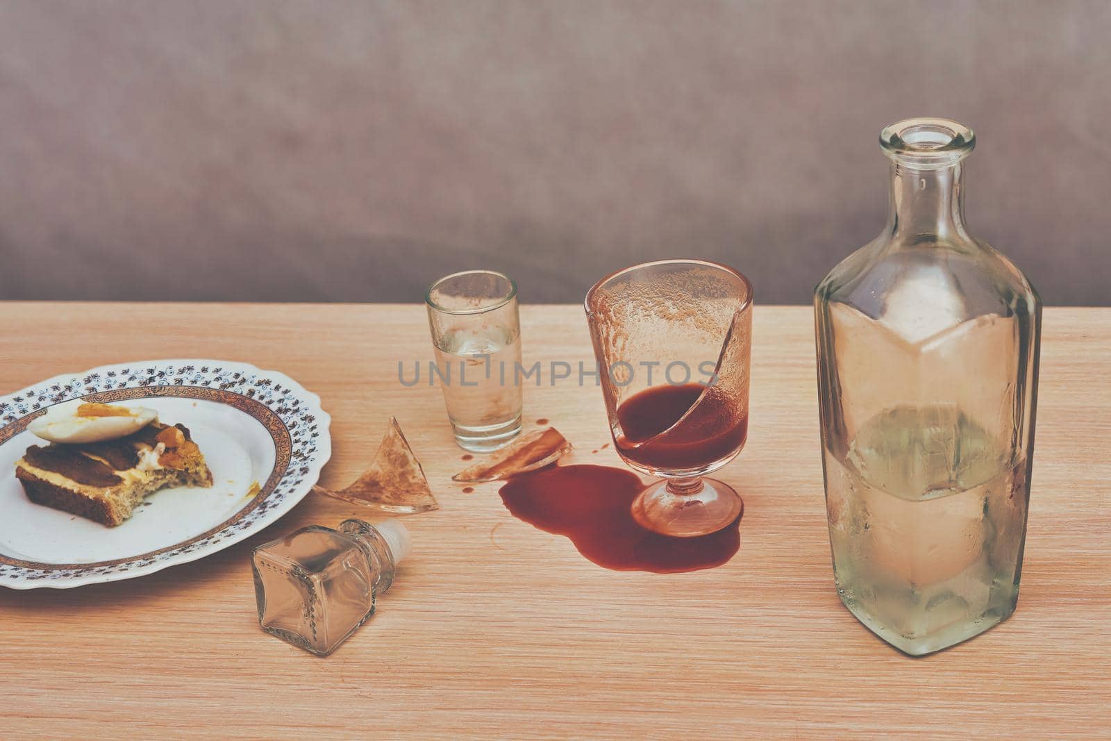 A broken glass and red tomato juice spilled on the table next to bottle of vodka. Concept drunkenness and alcoholism. Toning