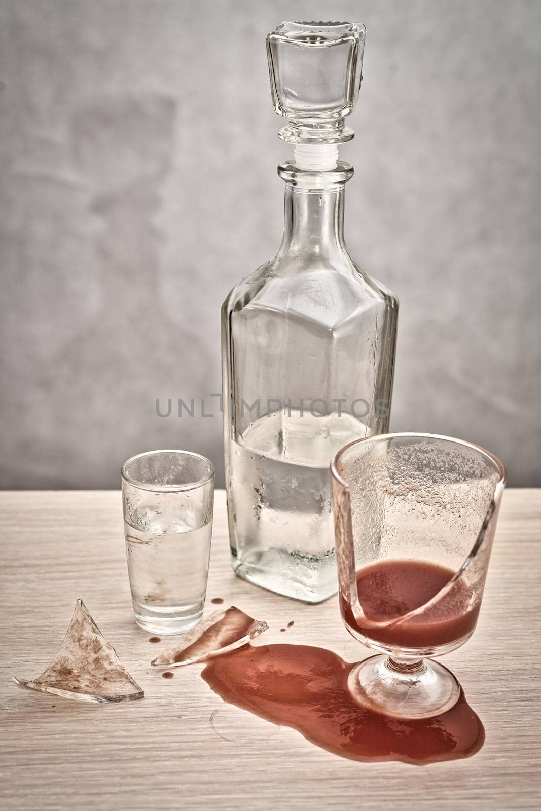 A broken glass and red tomato juice spilled on the table next to a bottle of vodka. Concept drunkenness and alcoholism