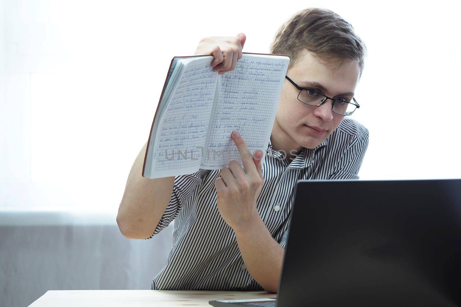 Online education. A student with glasses behind a laptop with a notebook. High quality photo