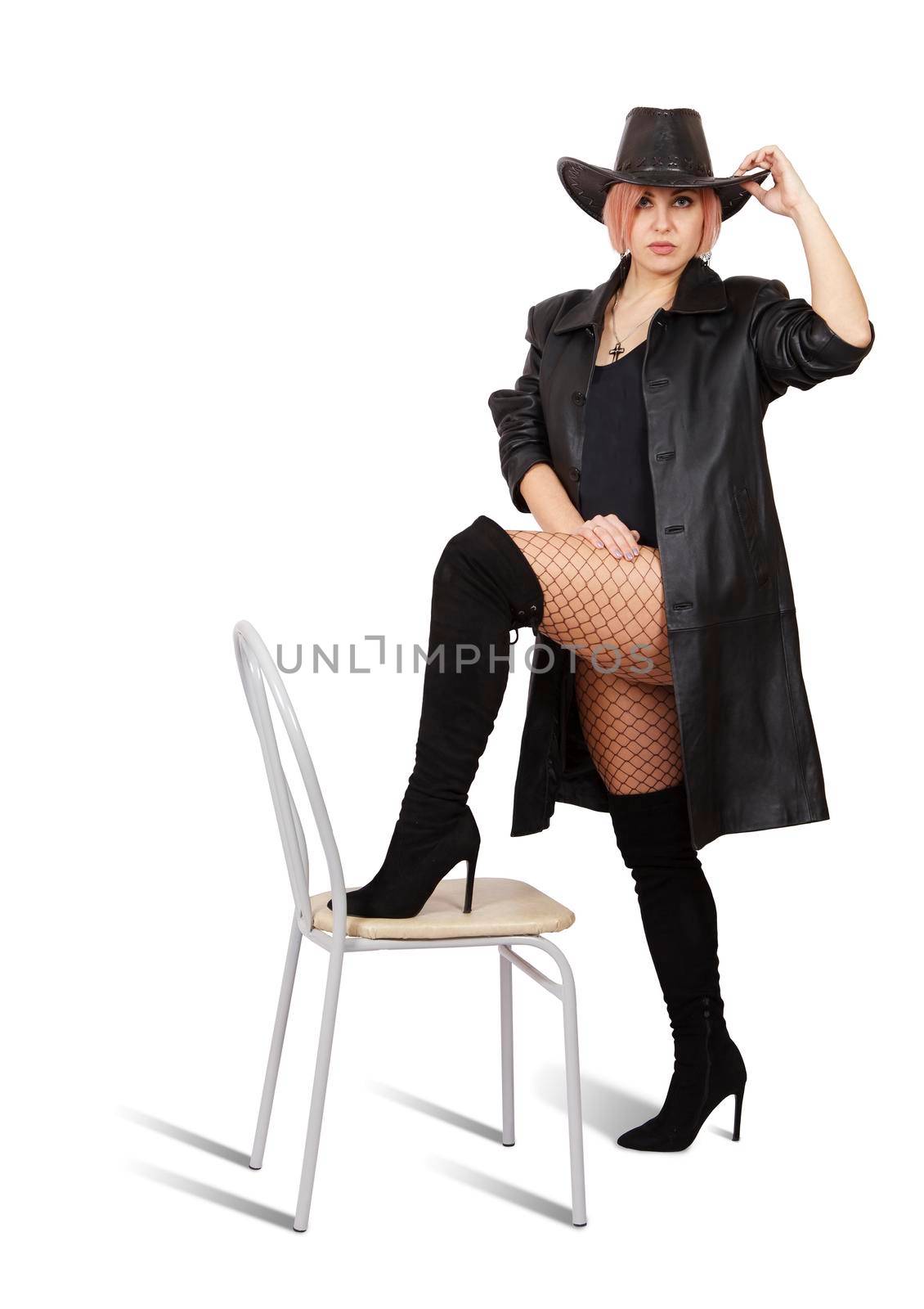 woman in leather coat, black hat, mesh tights and boots posing standing with her foot on a chair by raddnatt