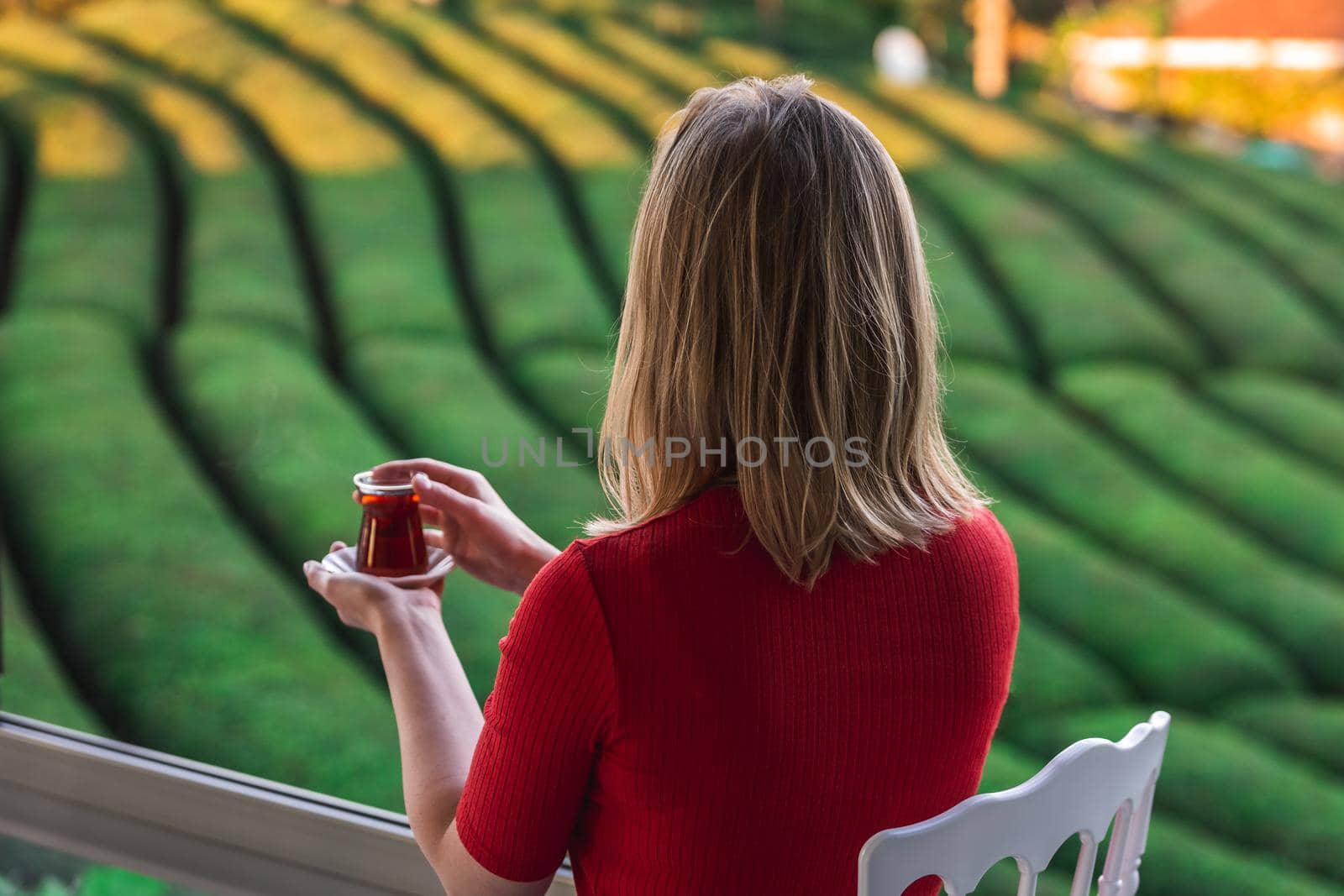 Beautiful lady in a red blouse holding traditional tea cup full with local hot beverage at the tea plantation in Haremtepe Ceceva village, Rize, Turkey.