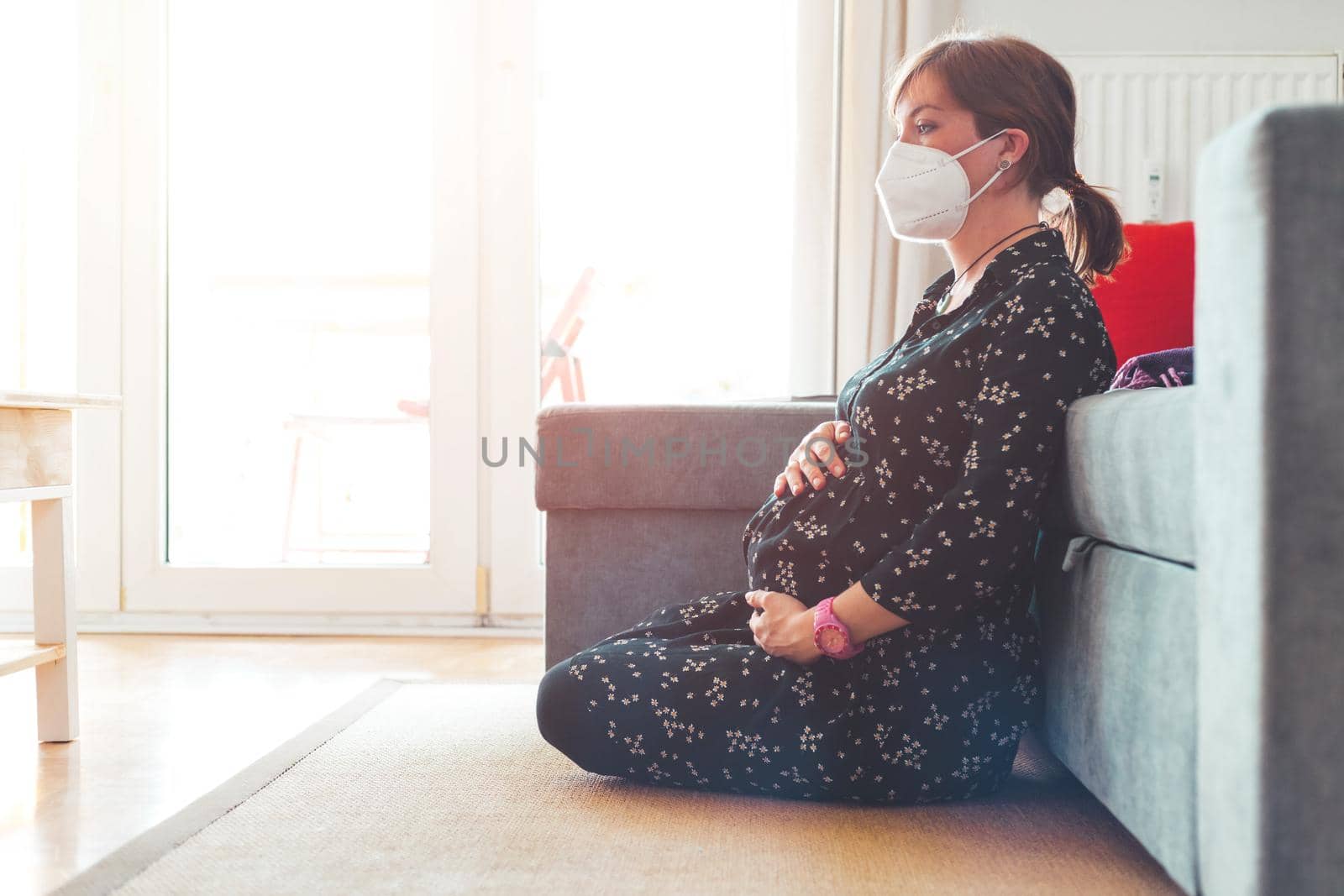 Pregnant woman with ffp2 face mask is sitting on the floor.
