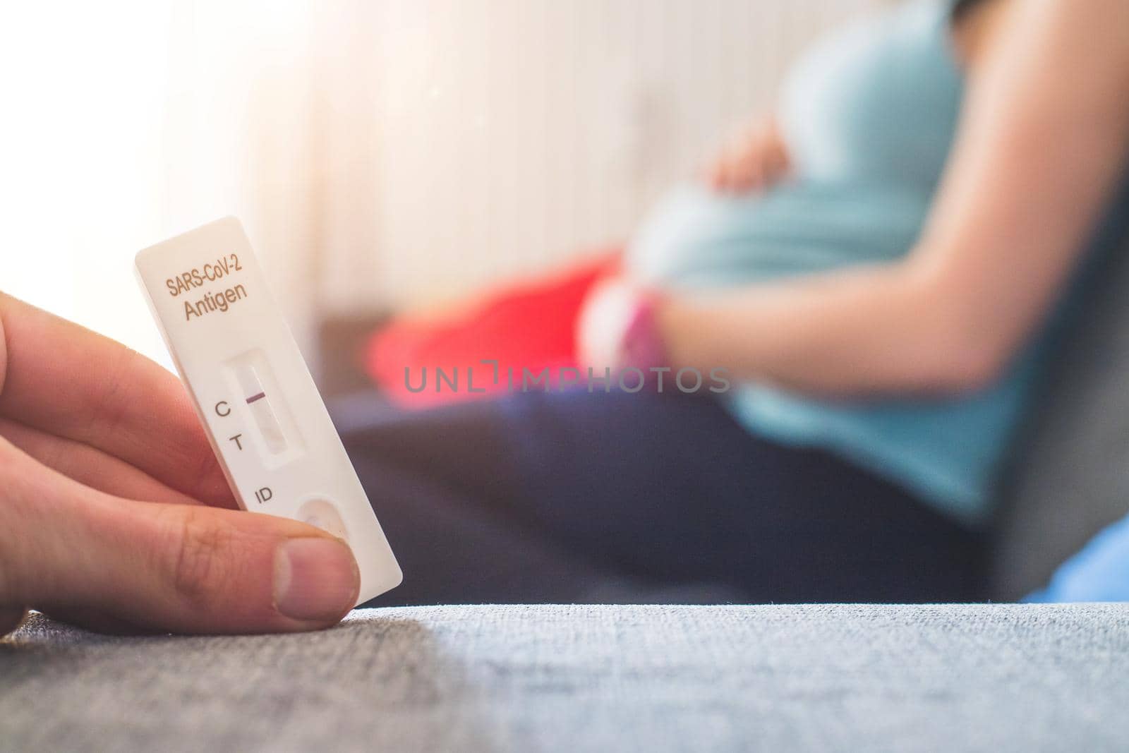 Close up of fingers holding express antigen covid test, negative result. Pregnant woman in the blurry background