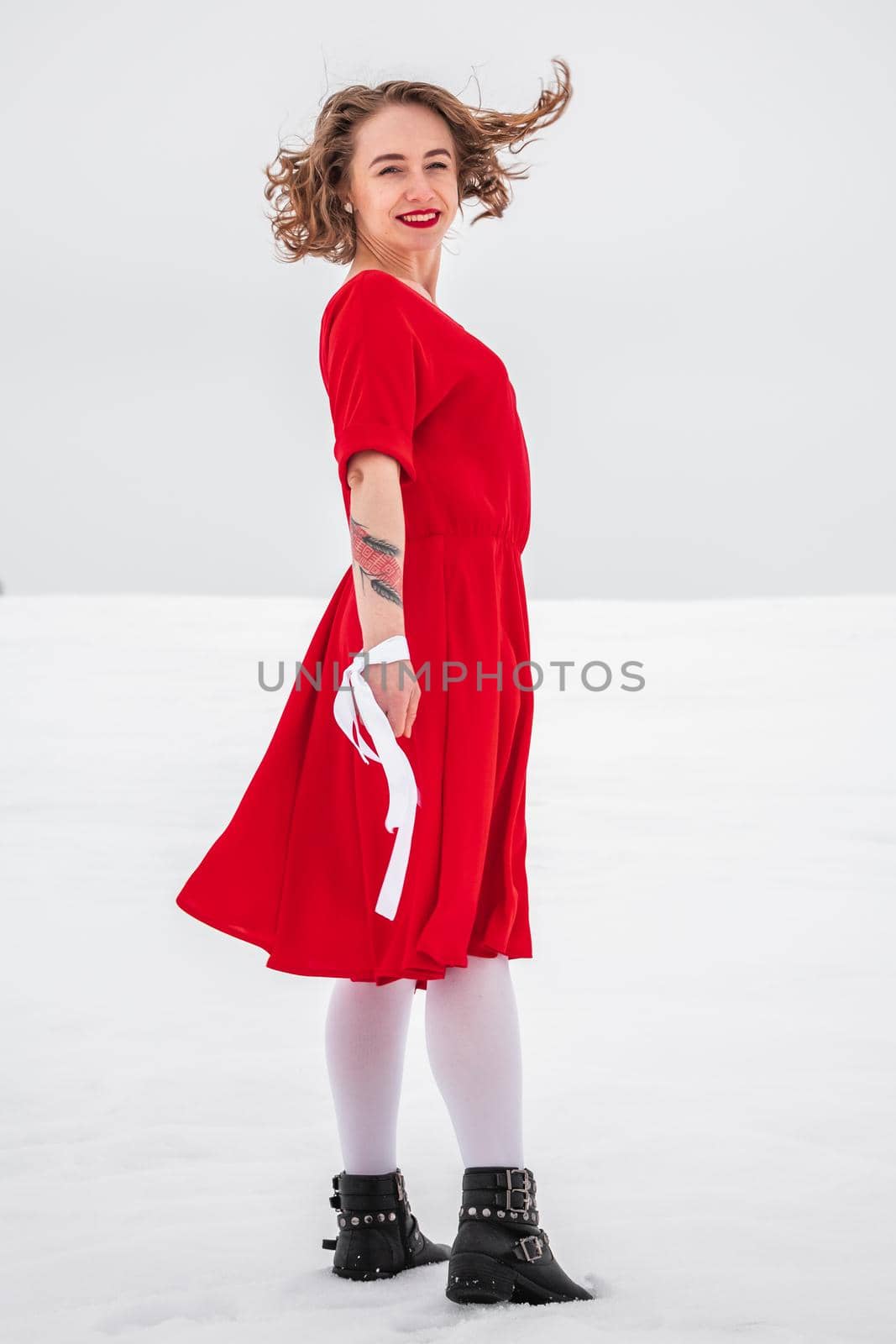 Beautiful woman in a red dress posing outside on a snowy field. She is wearing red dress and have tattoo on her arm.