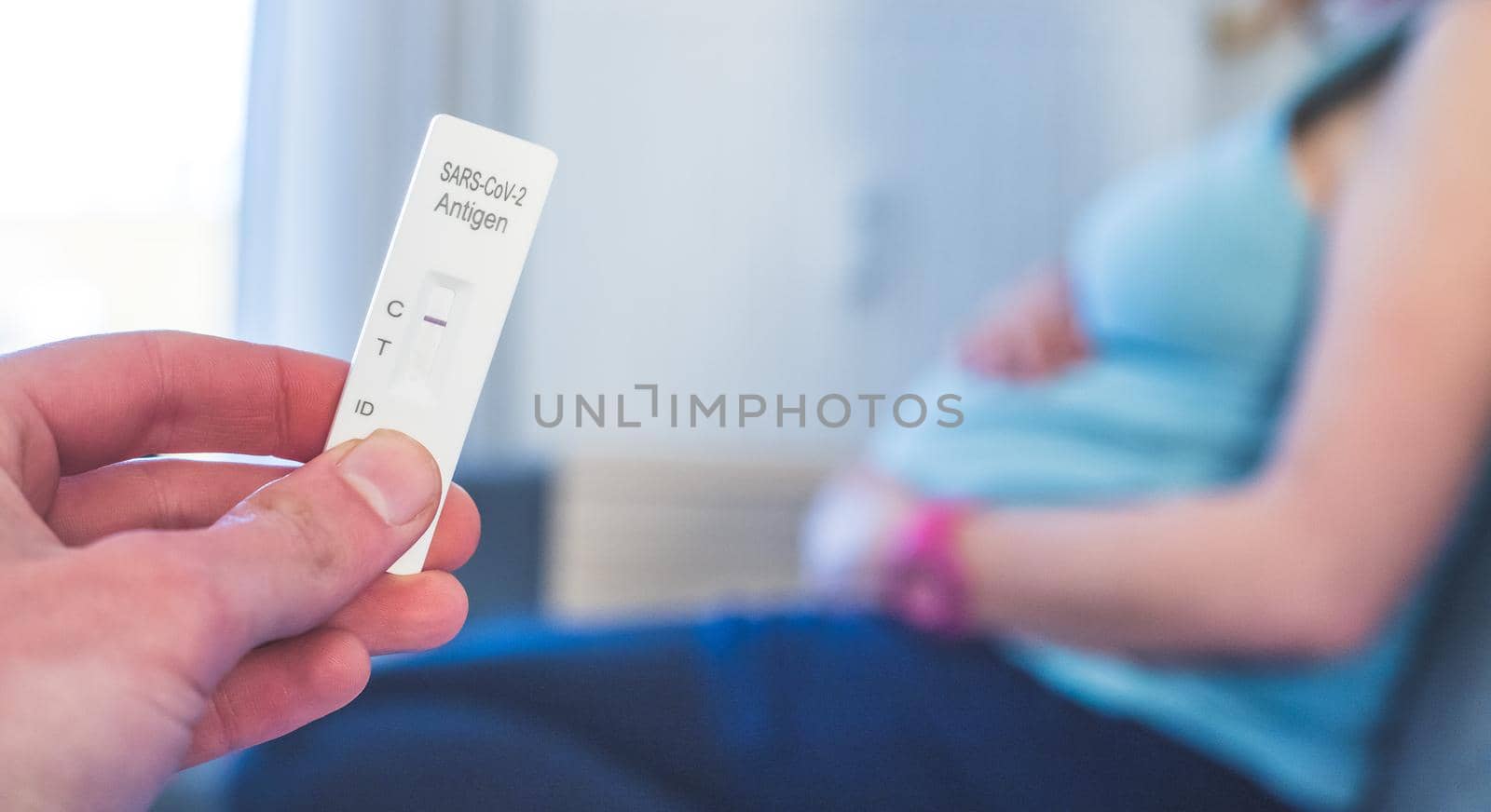 Close up of fingers holding express antigen covid test, negative result. Pregnant woman in the blurry background