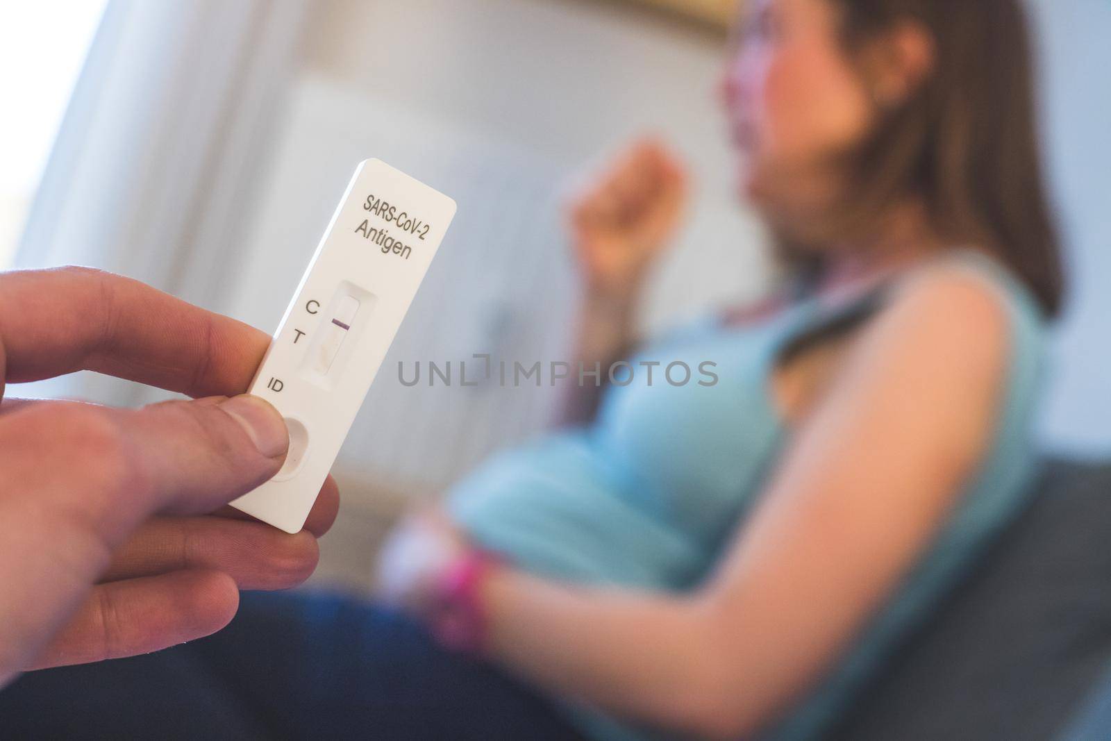 Close up of fingers holding express antigen covid test, negative result. Pregnant woman in the blurry background