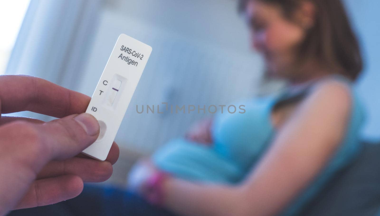 Close up of fingers holding express antigen covid test, negative result. Pregnant woman in the blurry background