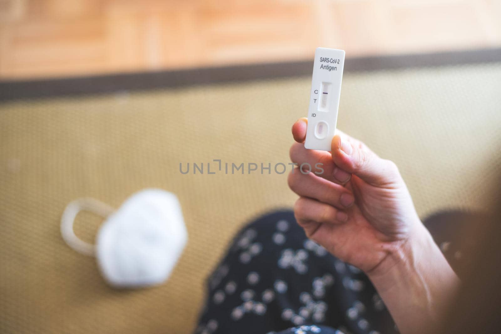 Express corona test at home: Close up of female fingers holding a negative covid antigen test, ffp2 mask in the background by Daxenbichler