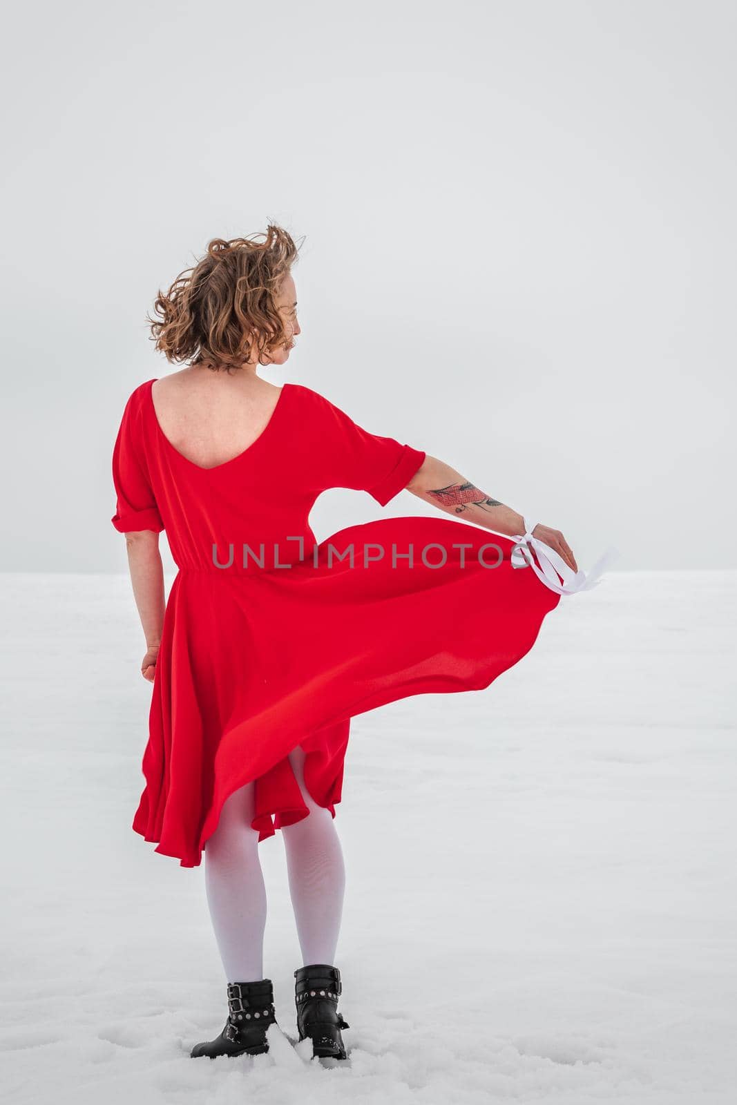 Beautiful woman in a red dress posing outside on a snowy field. She is wearing red dress and have tattoo on her arm.