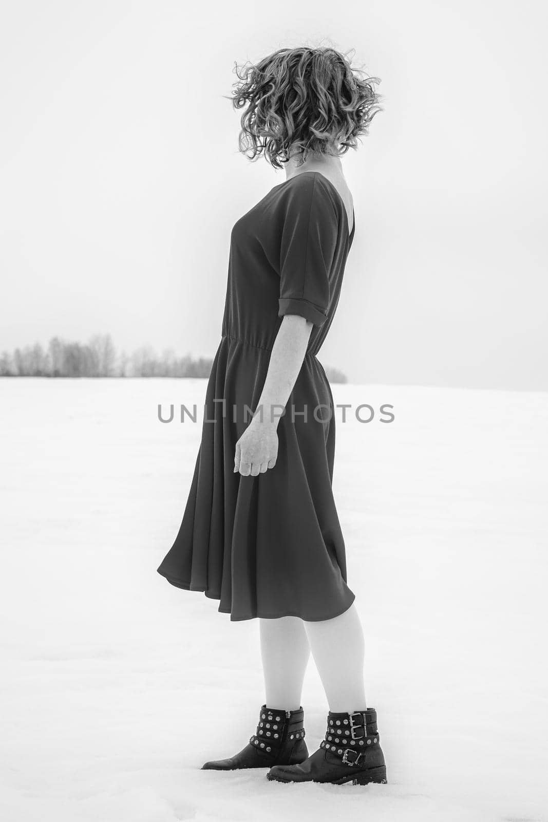 Beautiful woman in a red dress posing outside on a snowy field. She is wearing red dress and have tattoo on her arm.