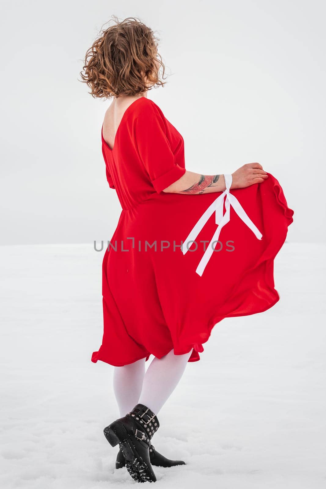 Beautiful woman in a red dress posing outside on a snowy field. She is wearing red dress and have tattoo on her arm.