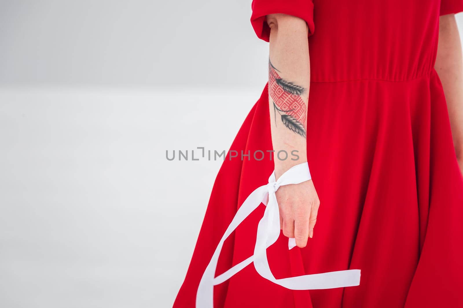 Beautiful woman in a red dress posing outside on a snowy field. She is wearing red dress and have tattoo on her arm.