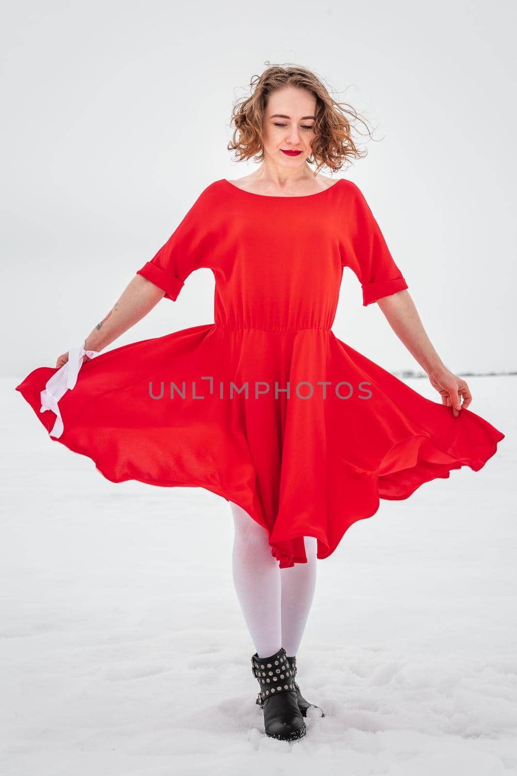 Beautiful woman in a red dress posing outside on a snowy field. She is wearing red dress and have tattoo on her arm.