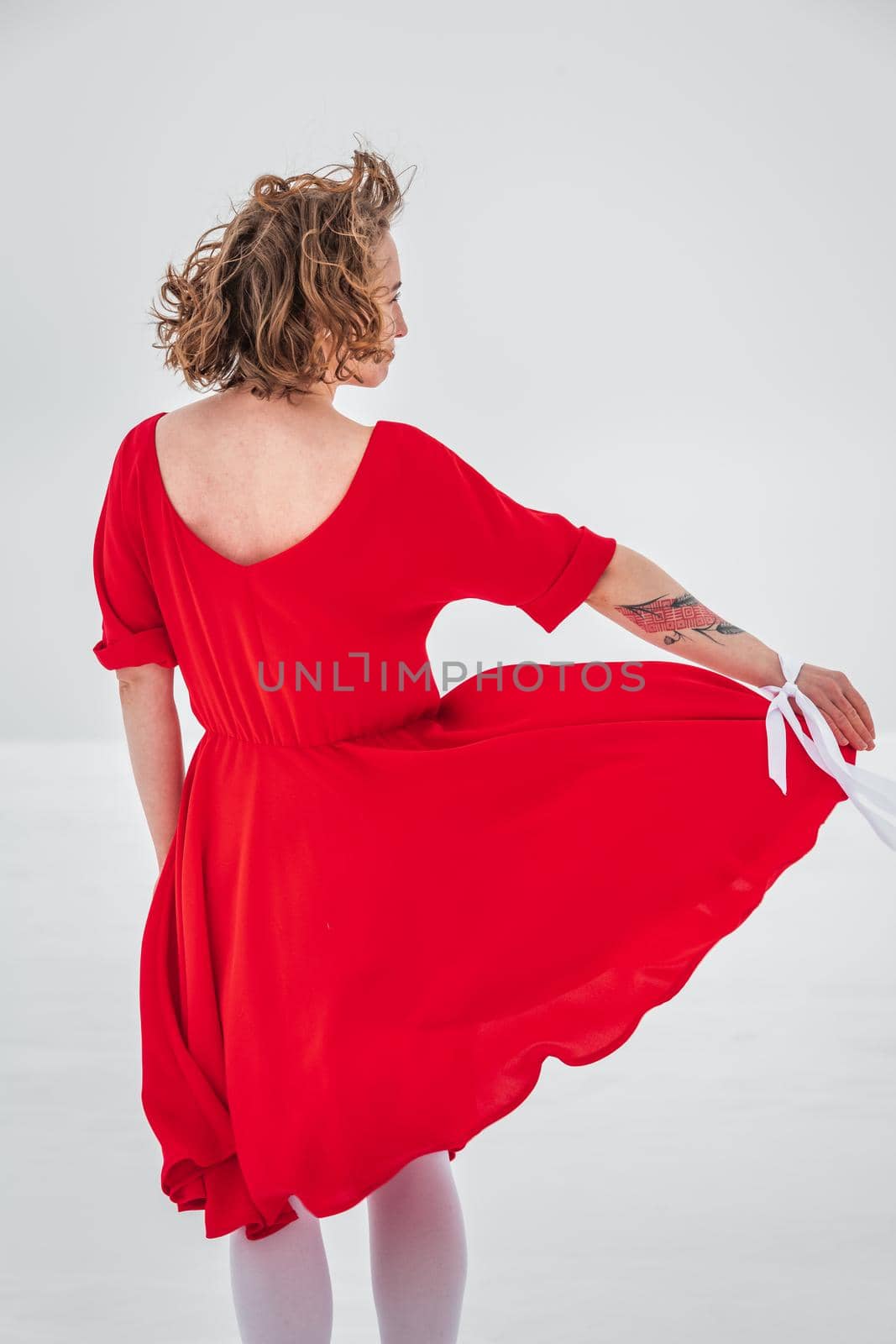 Beautiful woman in a red dress posing outside on a snowy field. She is wearing red dress and have tattoo on her arm.