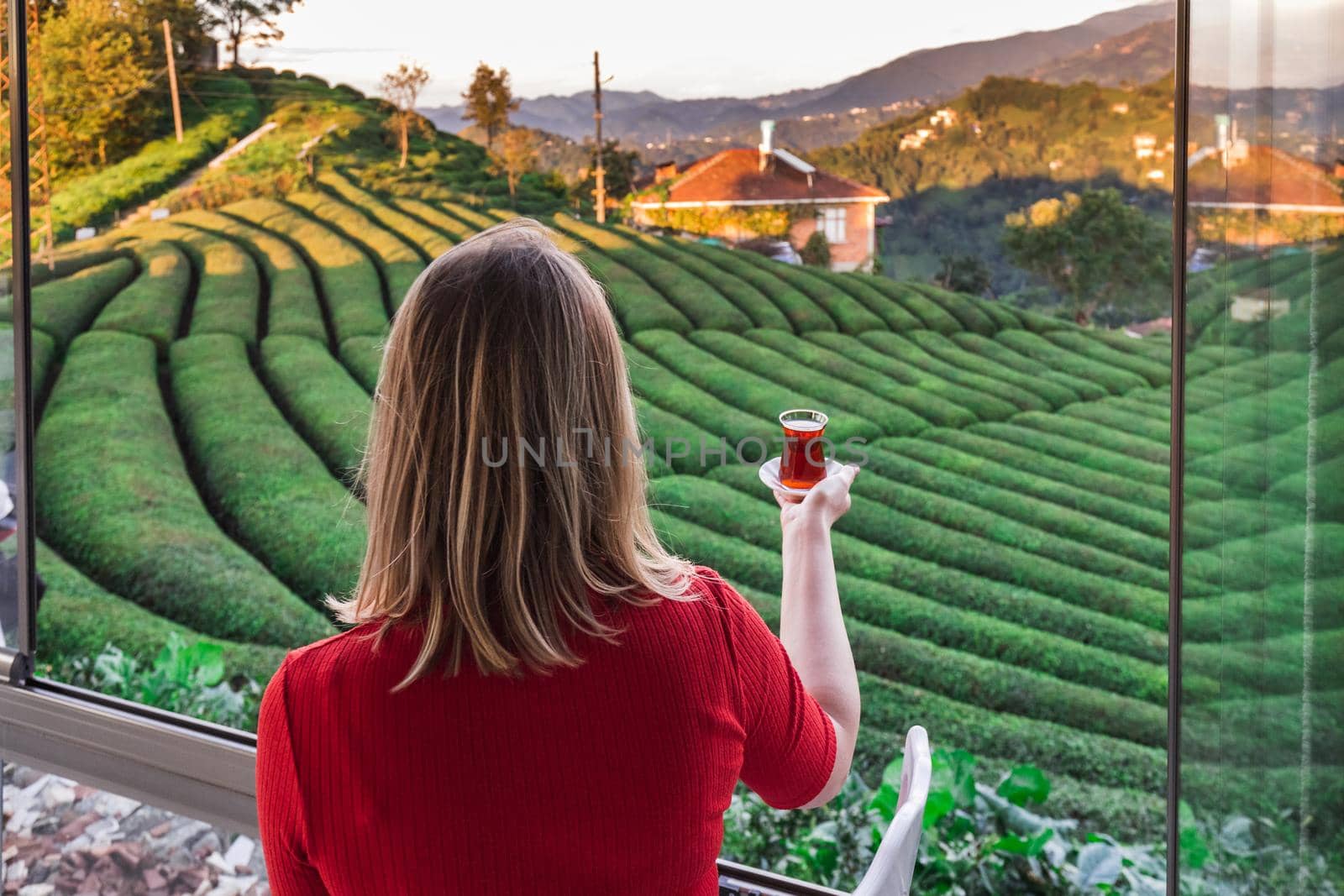 Beautiful lady in a red blouse holding traditional tea cup full with local hot beverage at the tea plantation in Haremtepe Ceceva village, Rize, Turkey.