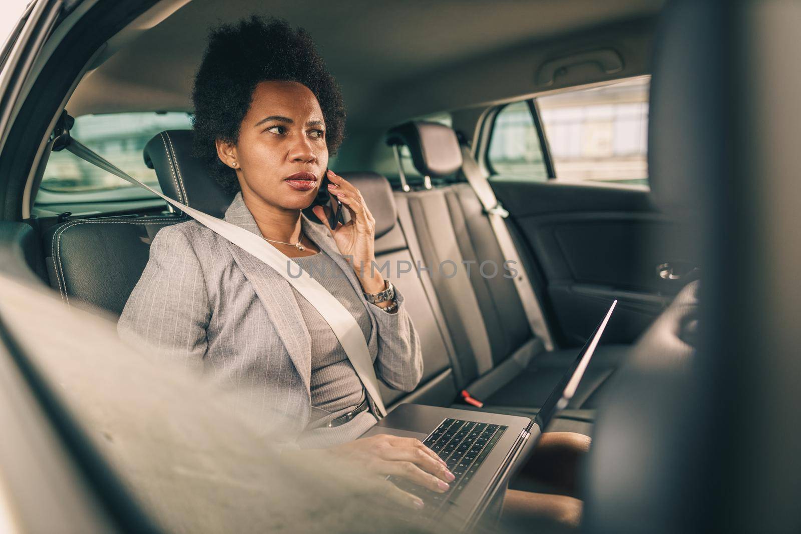 Shot of a worried black businesswoman talking on a smartphone while sitting in the backseat of a car during her morning commute.