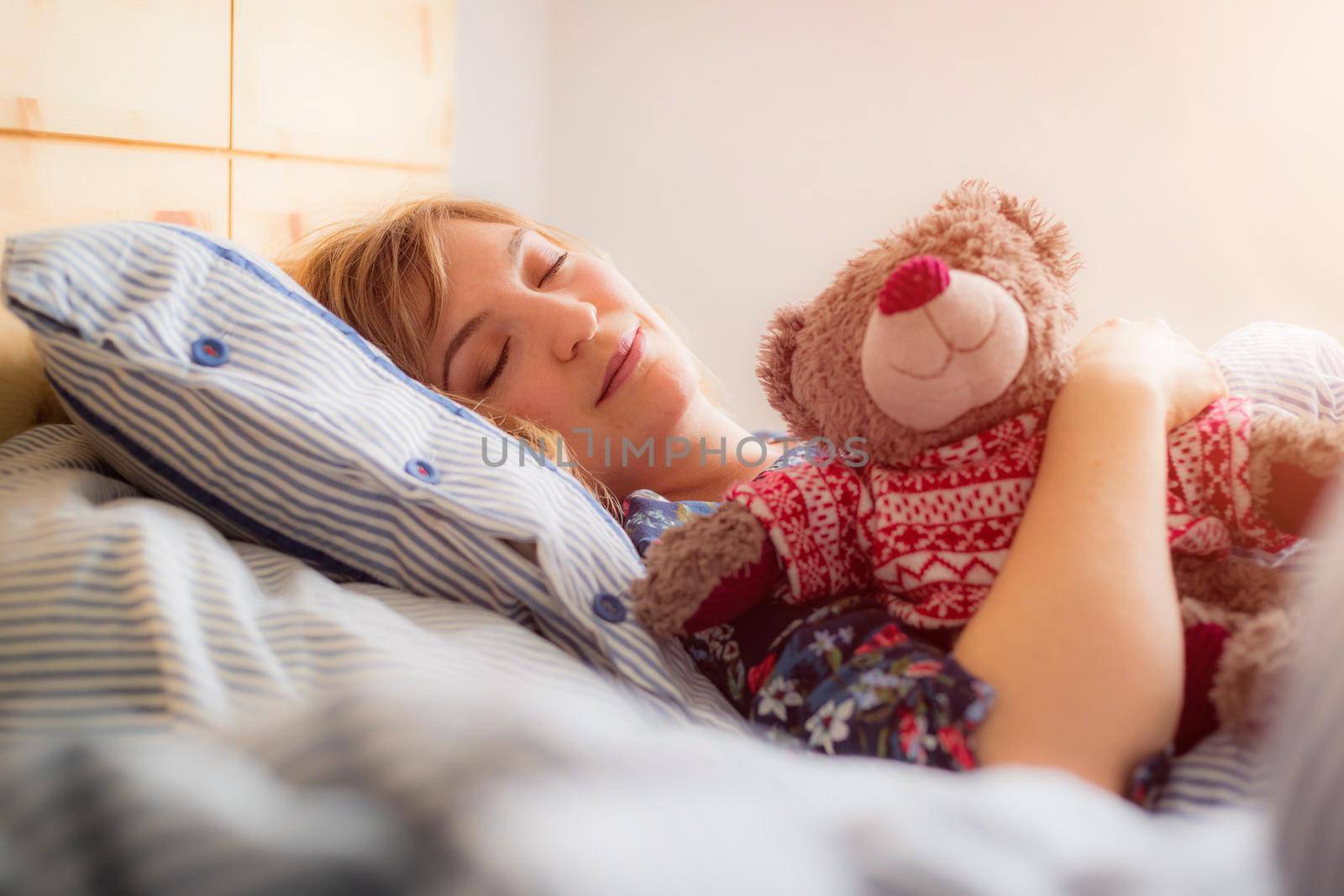 Young woman is sleeping peacefully with her teddy bear in her bedroom