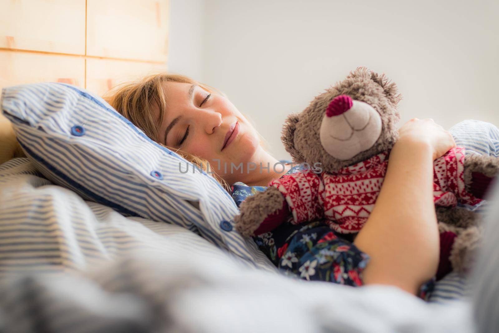 Young woman is sleeping peacefully with her teddy bear in her bedroom