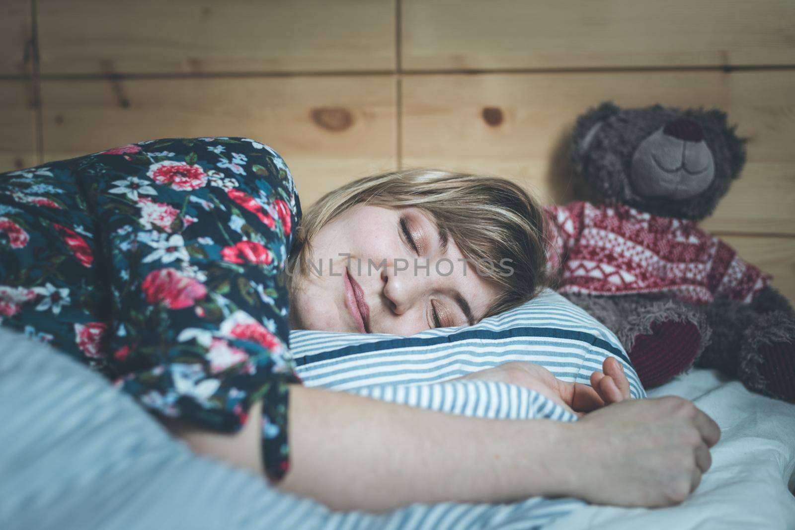 Restful sleep: Young female is sleeping in her bed, teddy bear by Daxenbichler