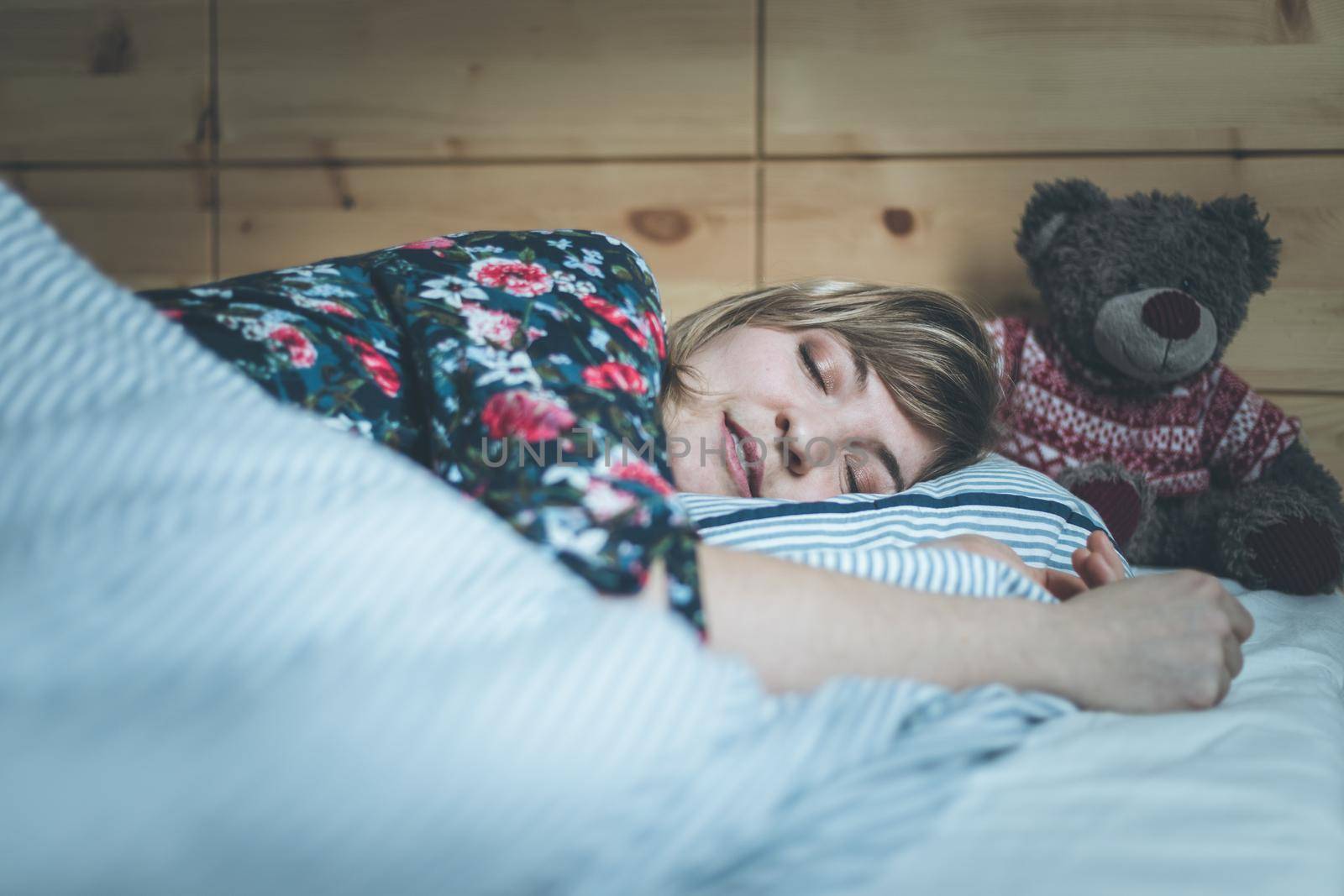 Young woman is sleeping peacefully with her teddy bear in her bedroom