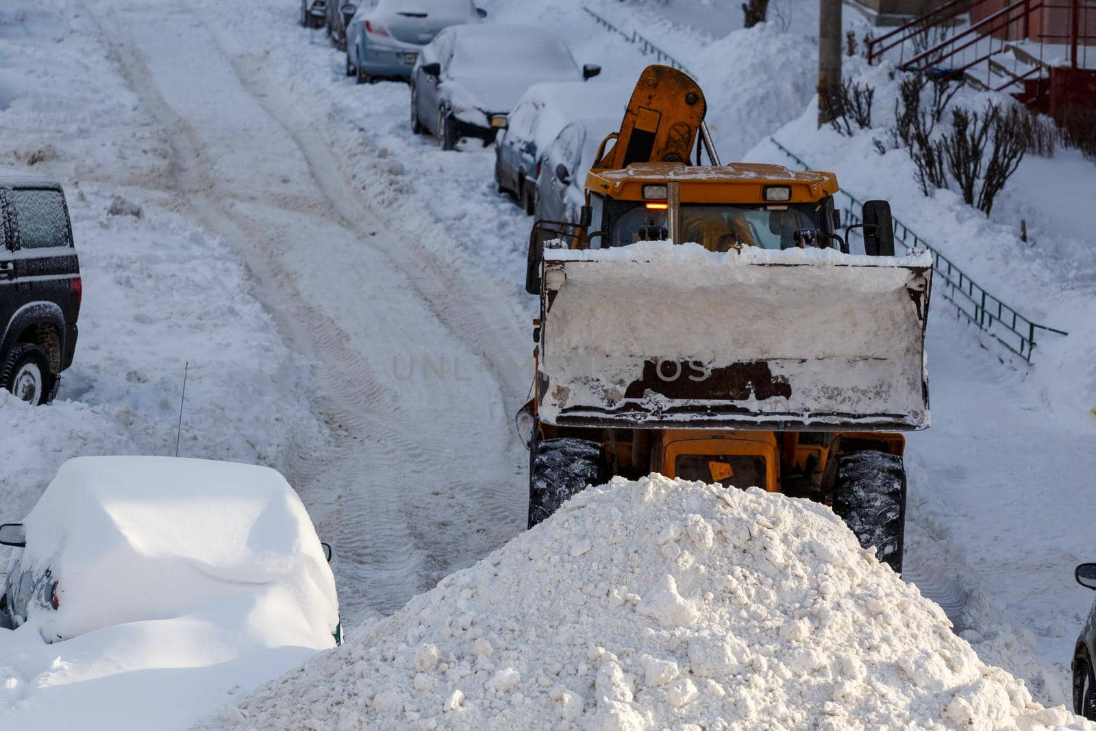 tractor removing snow from parking near residential building at winter daylight.