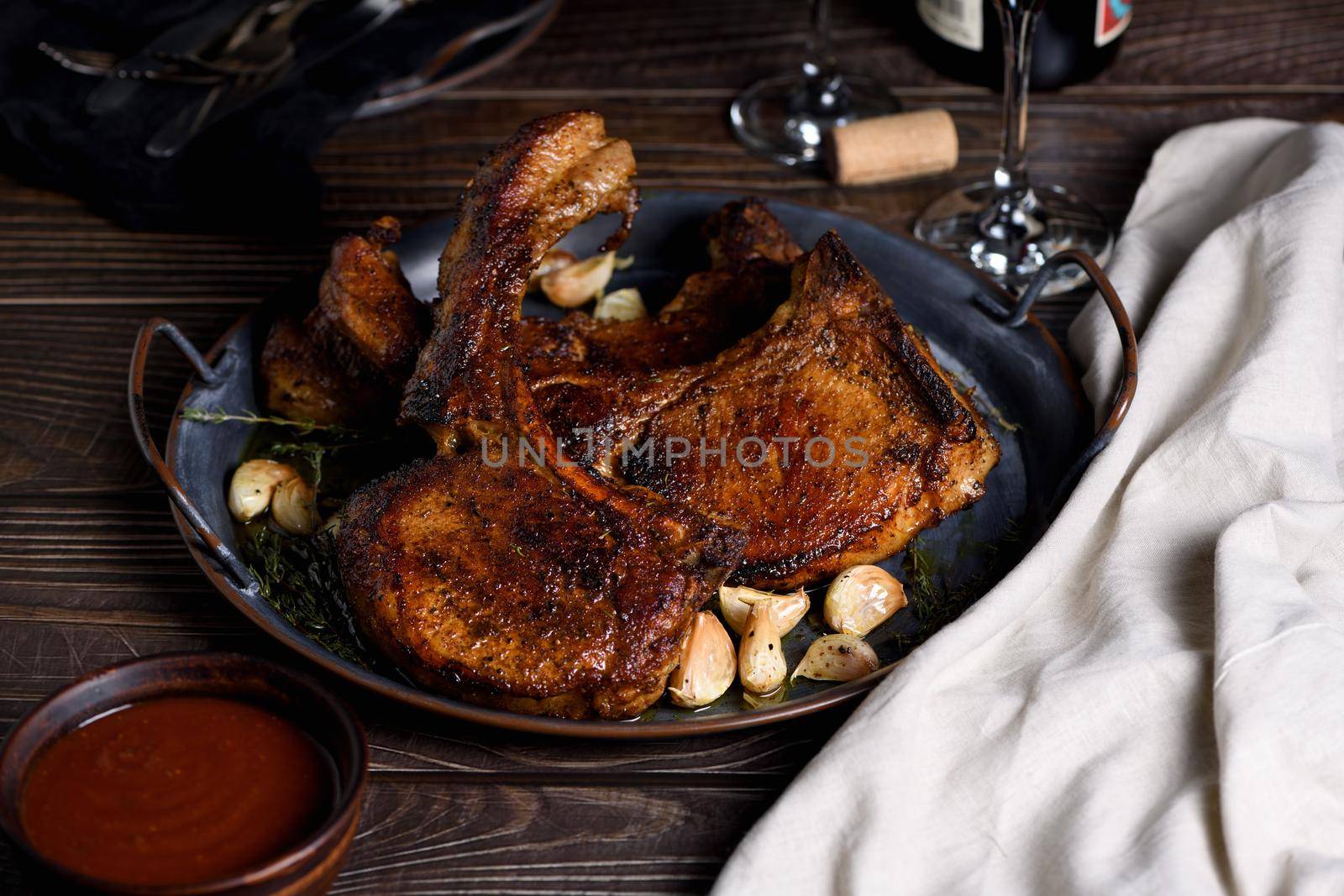 Juicy, slice of fried pork chop on a bone in oil with garlic and herbs in a pan. Close-up.