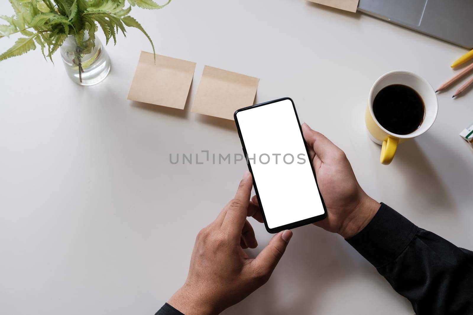 Close up of a man holding smartphone with blank screen mobile on wooden desk in home office, top view by itchaznong