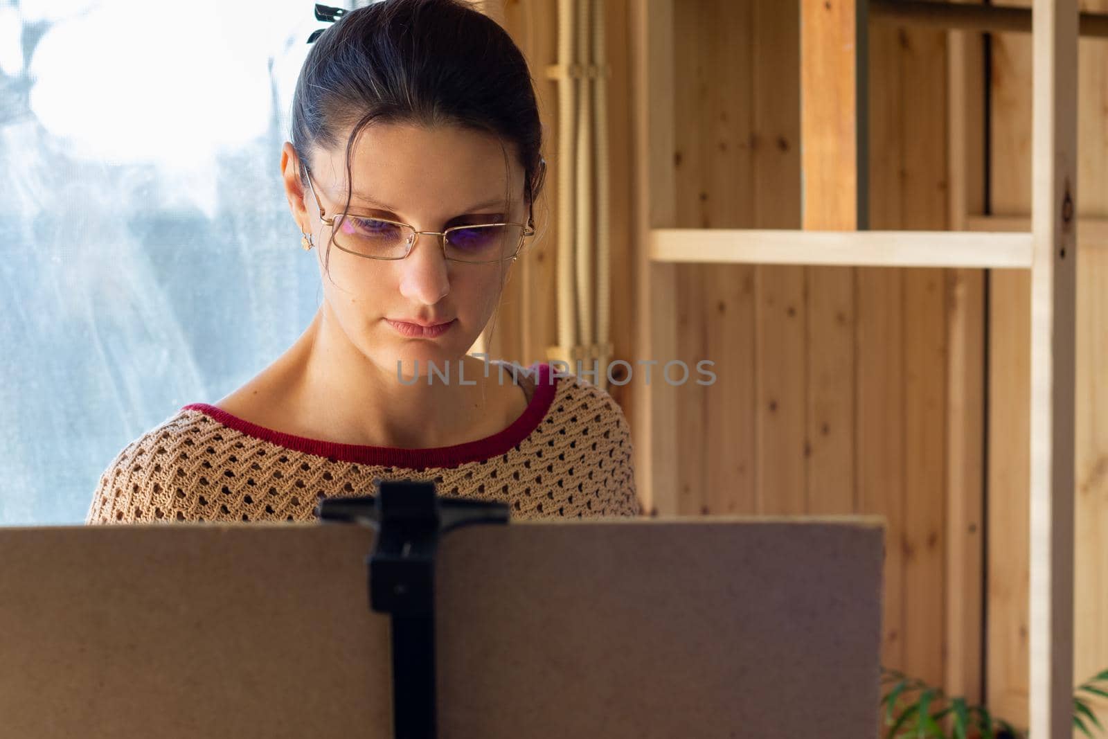Portrait of an artist at work, a girl draws a drawing on an easel by the window, close-up