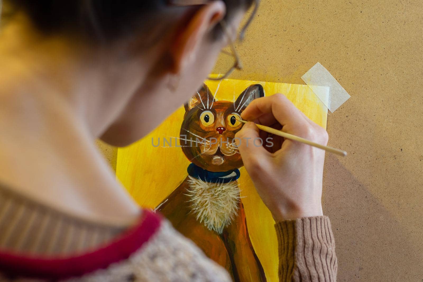 The artist paints a drawing of a cat on an easel with acrylic paints, a view from the artist's back