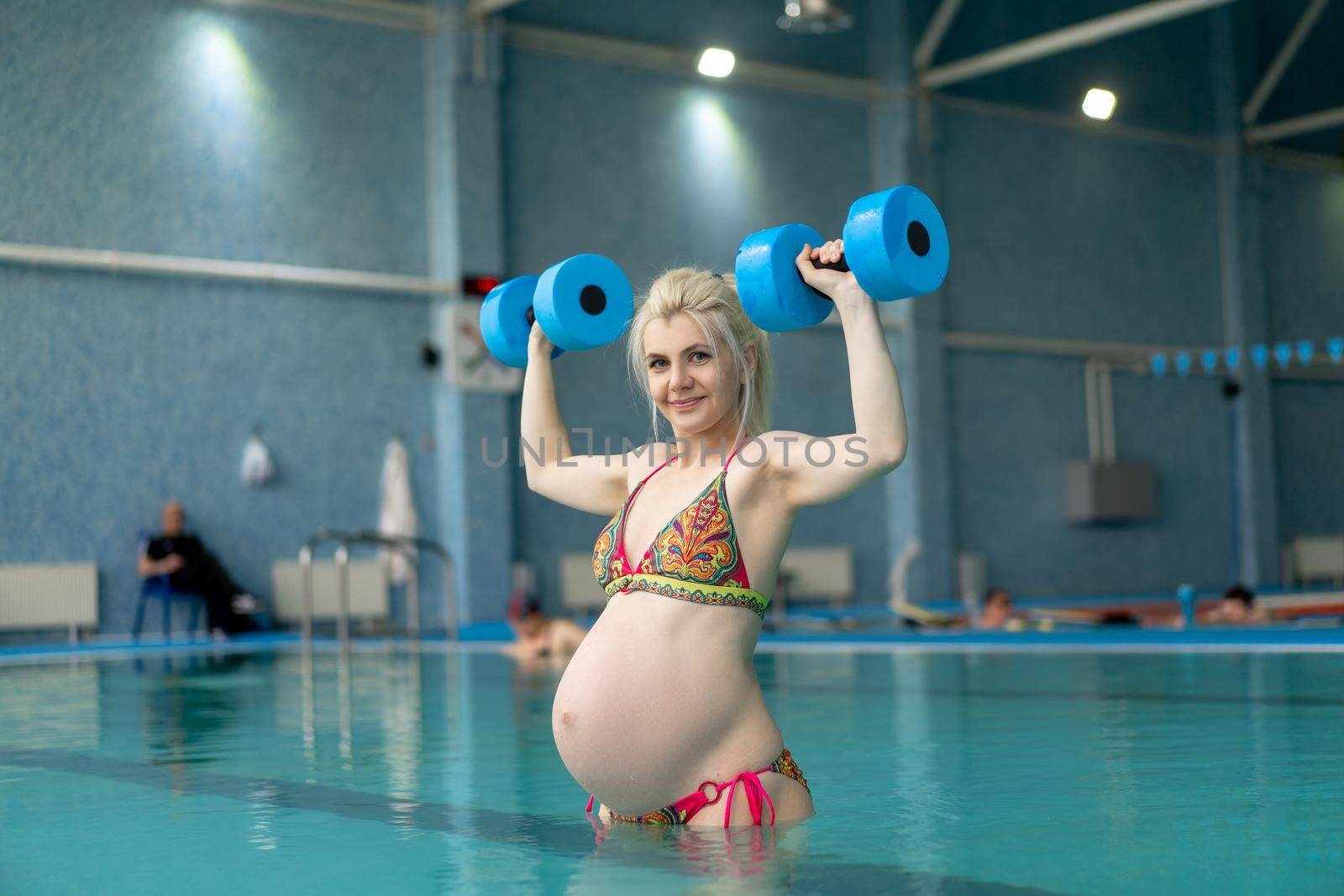 Pregnant woman standing in water with dumbbells indoors swiming pool Active pregnancy Sport and fitnes concept Helthy lifestyle