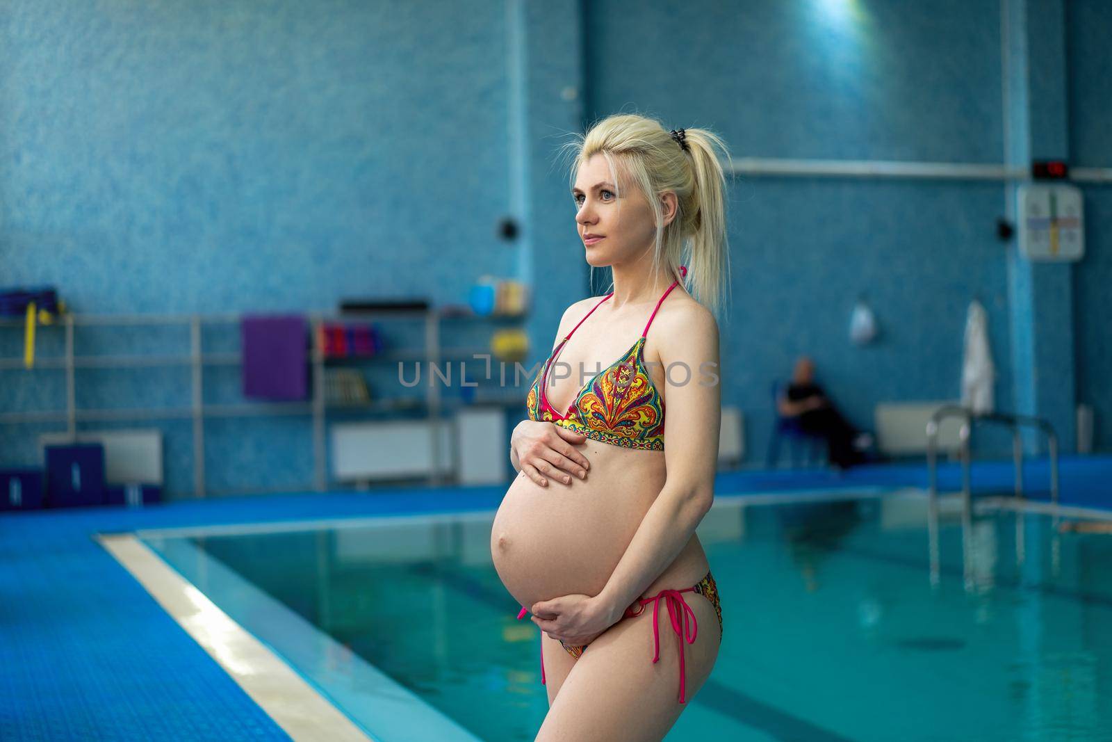 Pregnant woman standing indoors swiming pool hugg big tummy Active pregnancy Sport and fitnes concept Helthy lifestyle