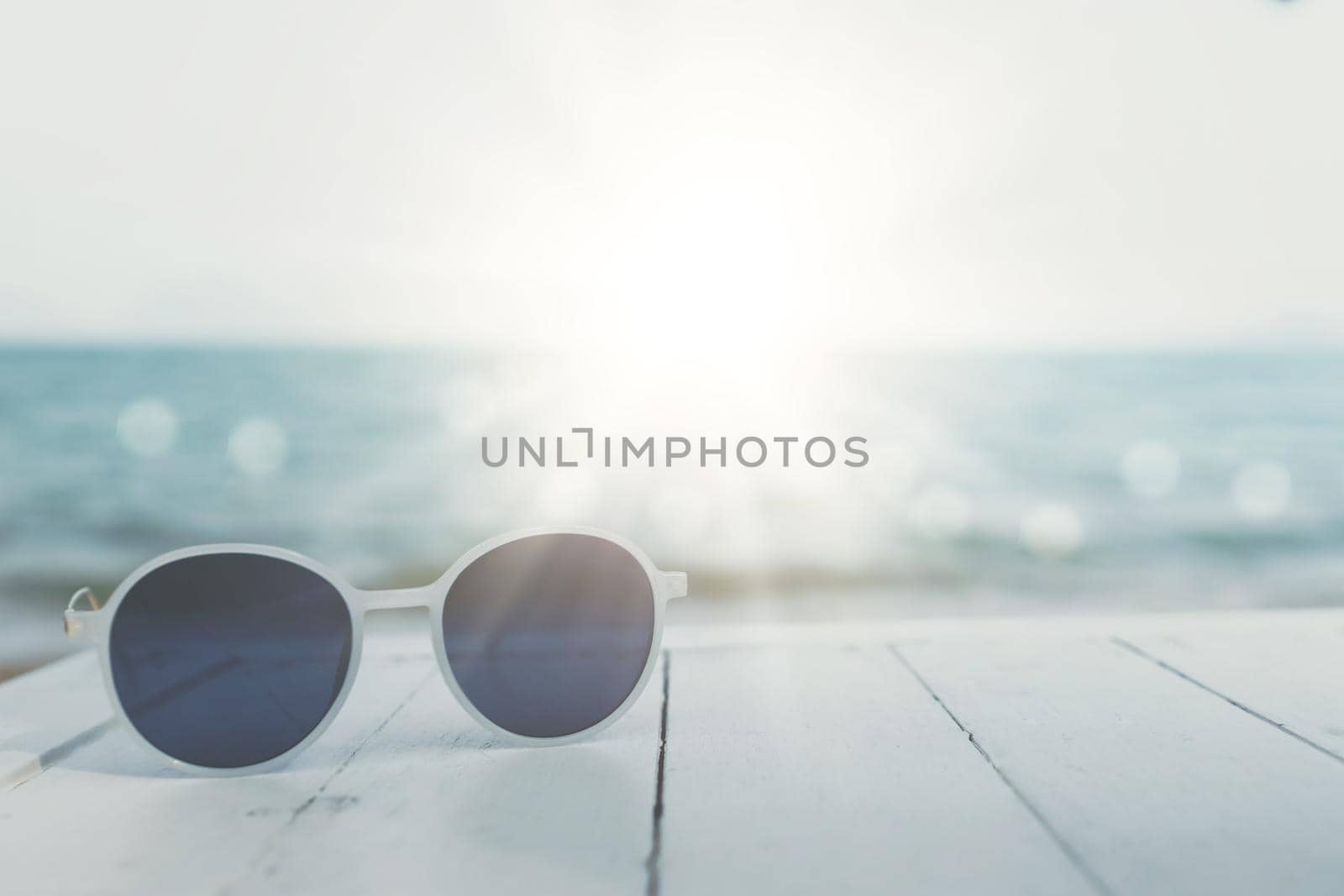 Selective focus of sunglasses on the table at summer beach resort with sunlight background. Holiday vacation travel tourism. by Suwant