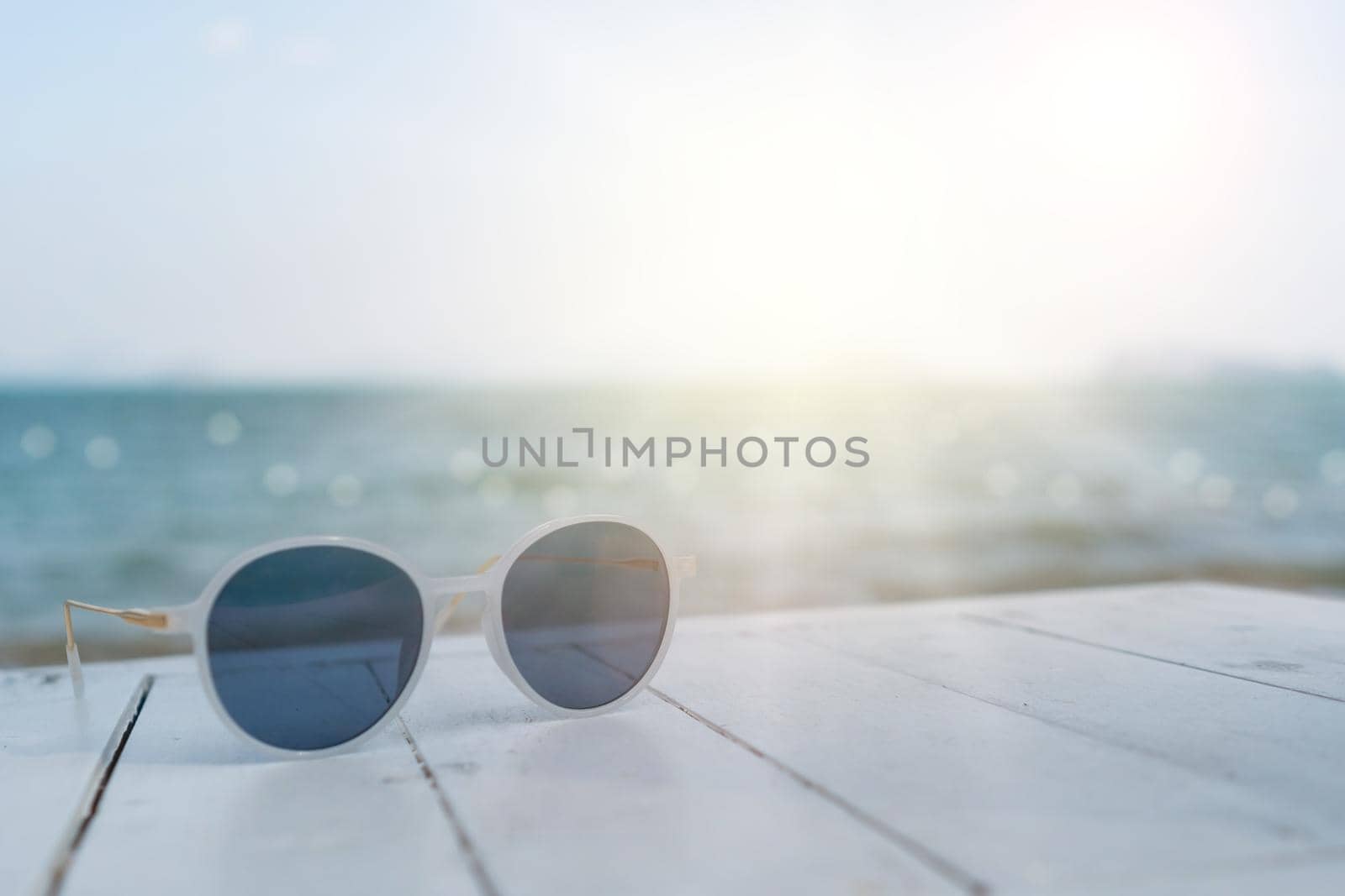 Selective focus of sunglasses on the table at summer beach resort with sunlight background. Holiday vacation travel tourism concept.