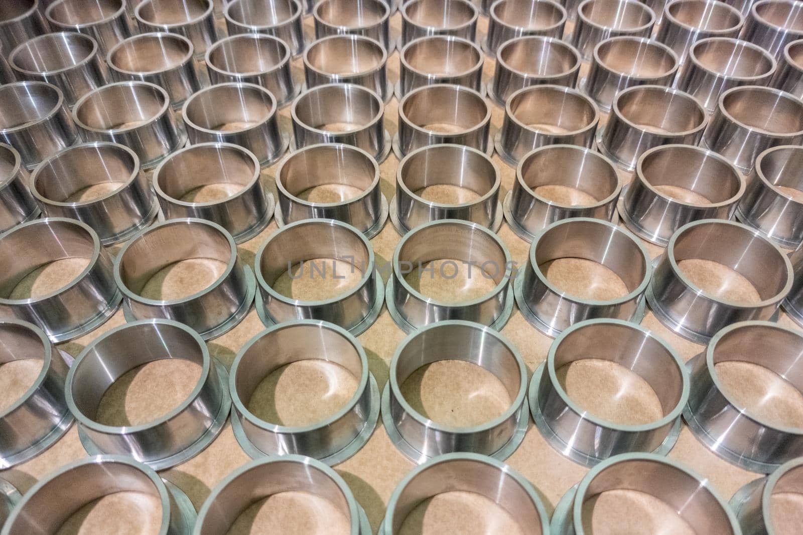 full frame batch of shiny steel cylindrical sleeve parts with flange - close-up with selective focus