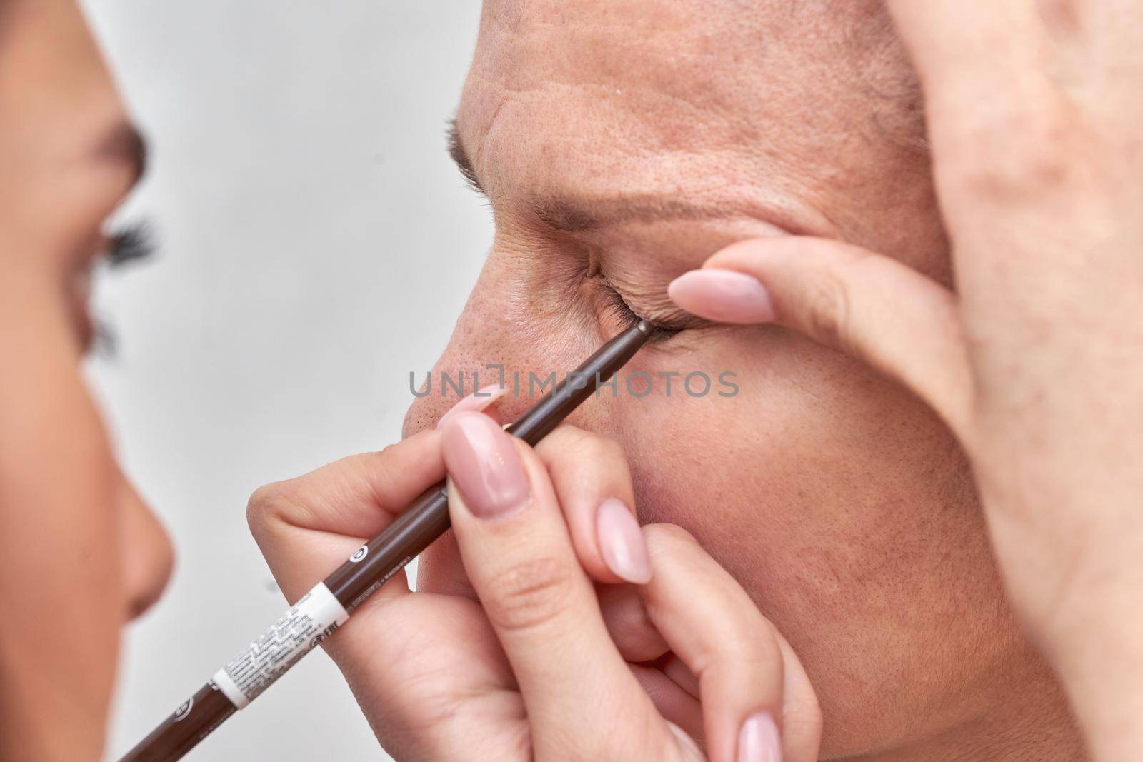 Woman at the reception at the beautician applies makeup. Master brings the eyebrows and eyelashes with a cosmetic pencil