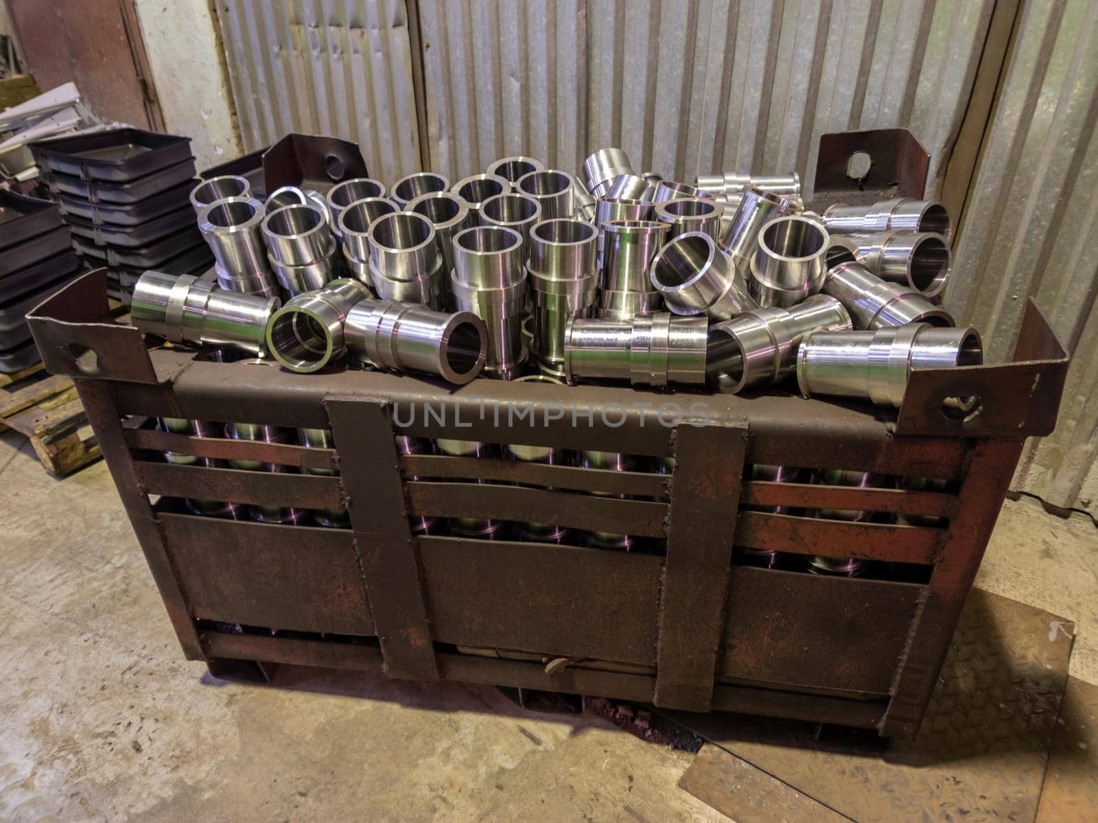 shiny steel cylindrical parts after turning operations overflowing big intermodal steel container box on factory floor