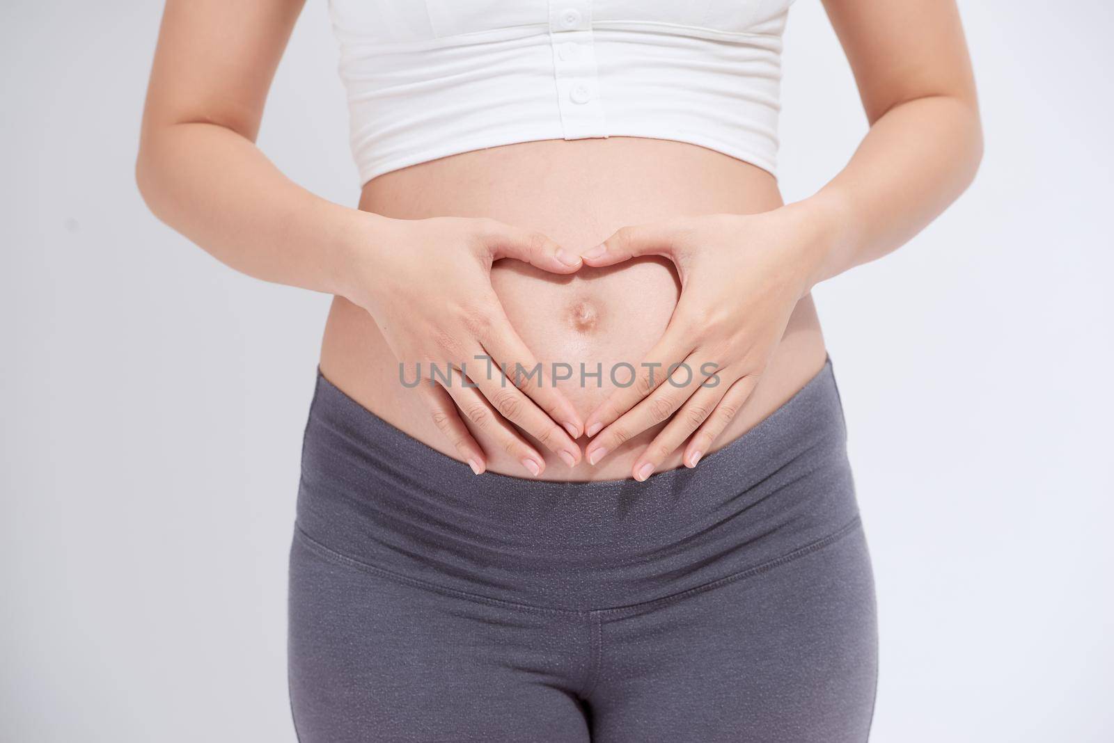 happy pregnant woman holding hands in heart shape on belly