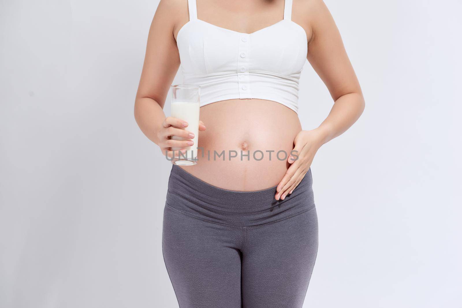 Happy pregnant woman drinking a glass of fresh milk and touching her belly  by makidotvn