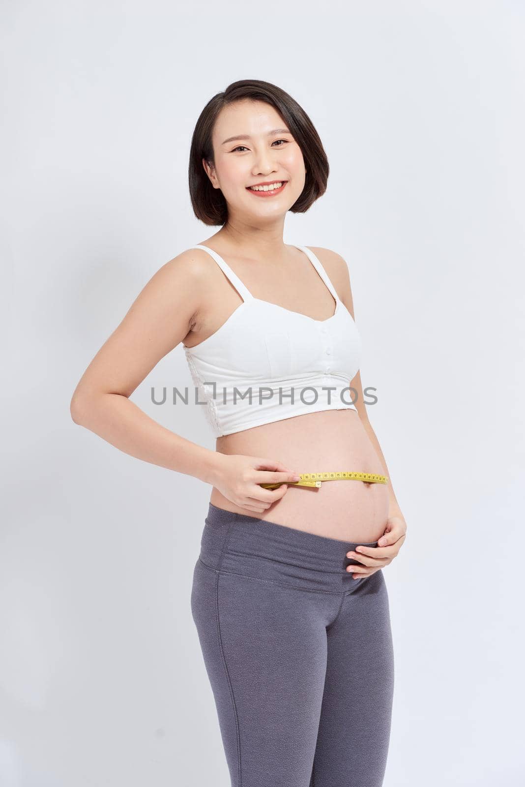 portrait of smiling pregnant woman measuring tummy with measuring tape isolated on white