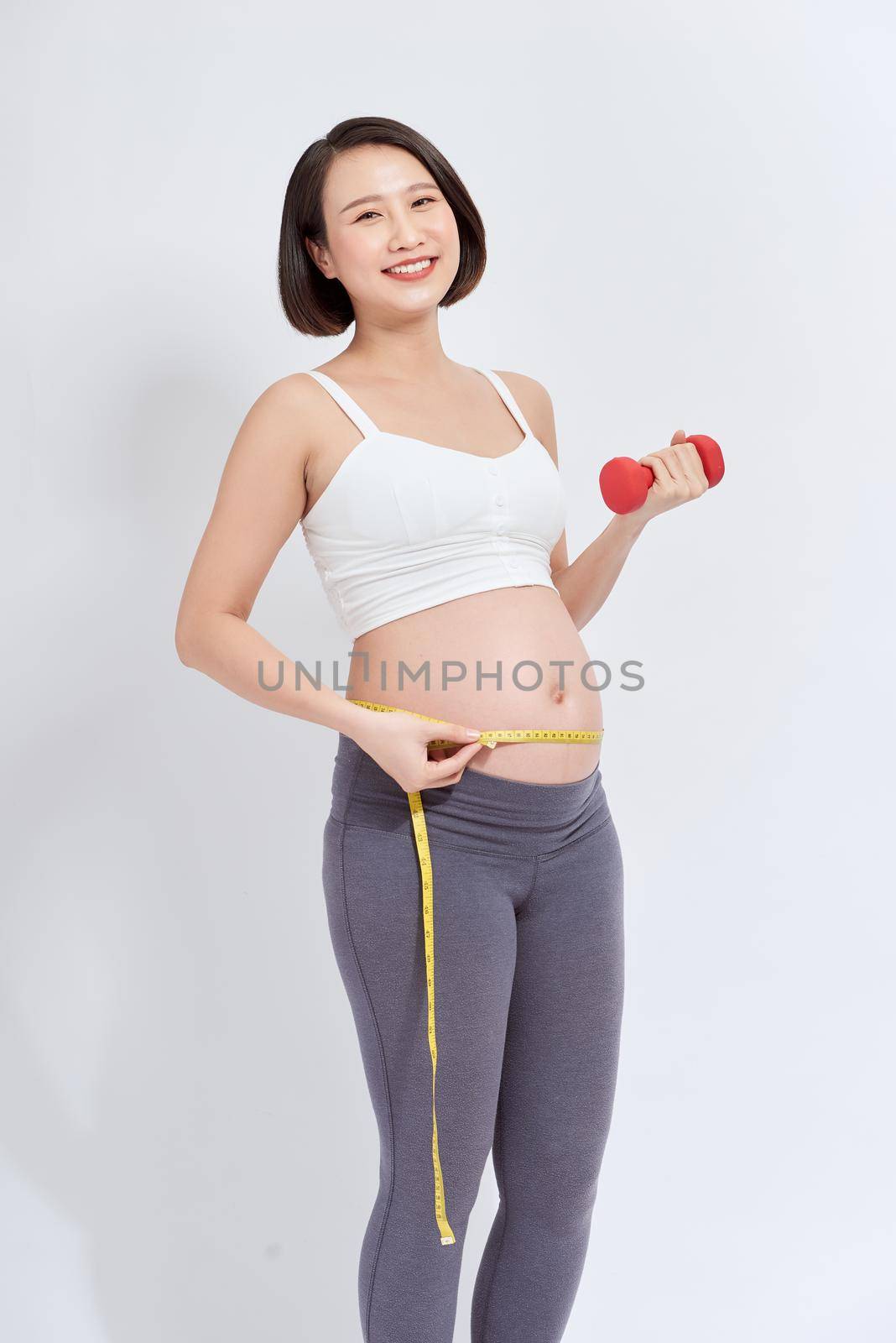 young pregnant woman doing fitness and measuring belly with measuring tape by makidotvn