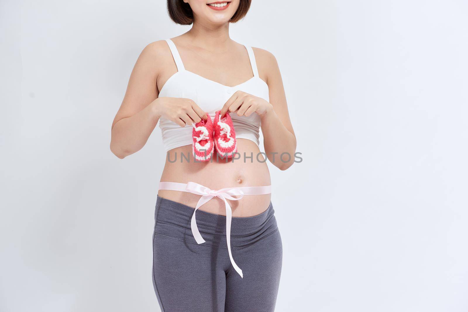 dreamy pregnant woman holding baby booties near tummy on white by makidotvn