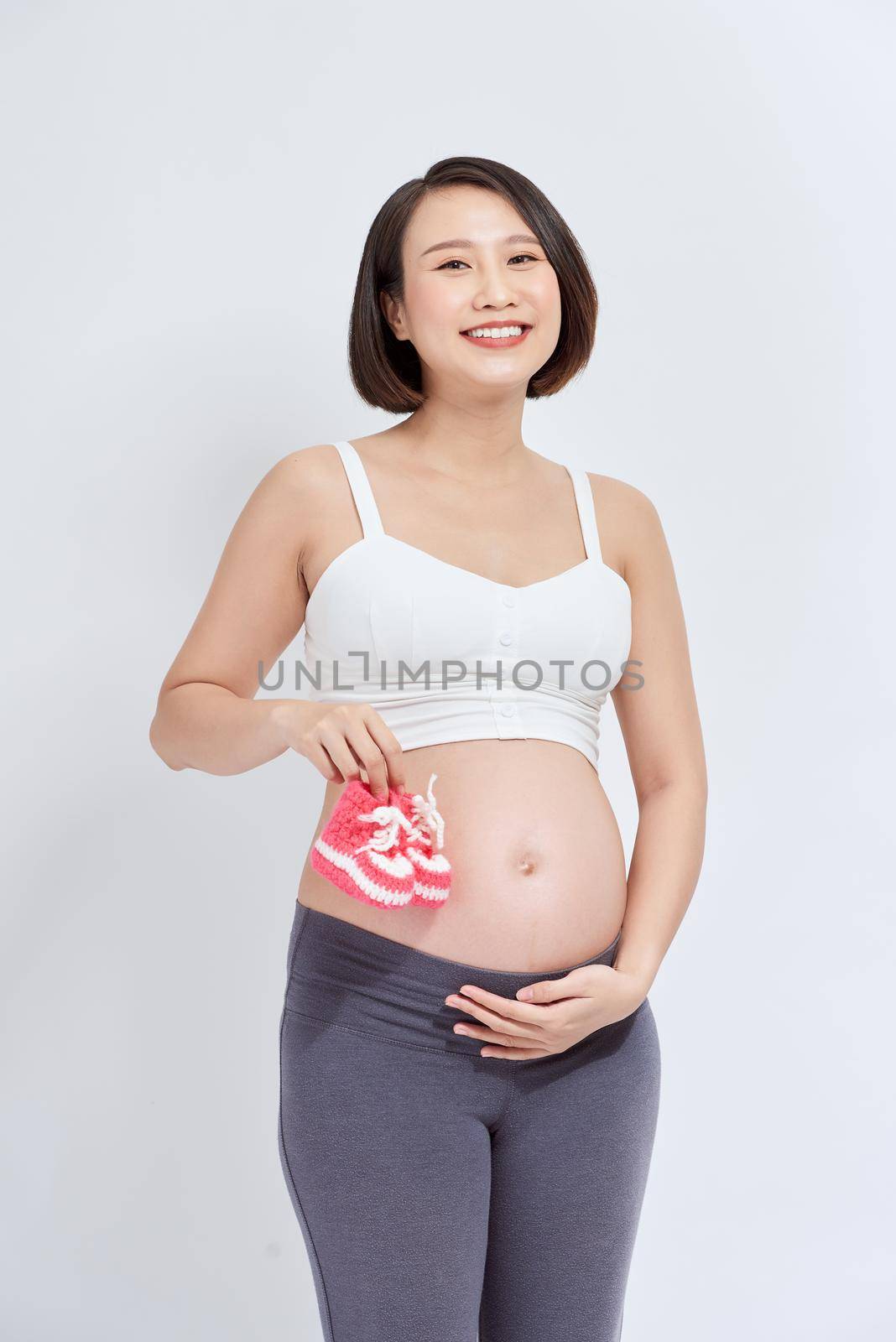 dreamy pregnant woman holding baby booties near tummy on white by makidotvn