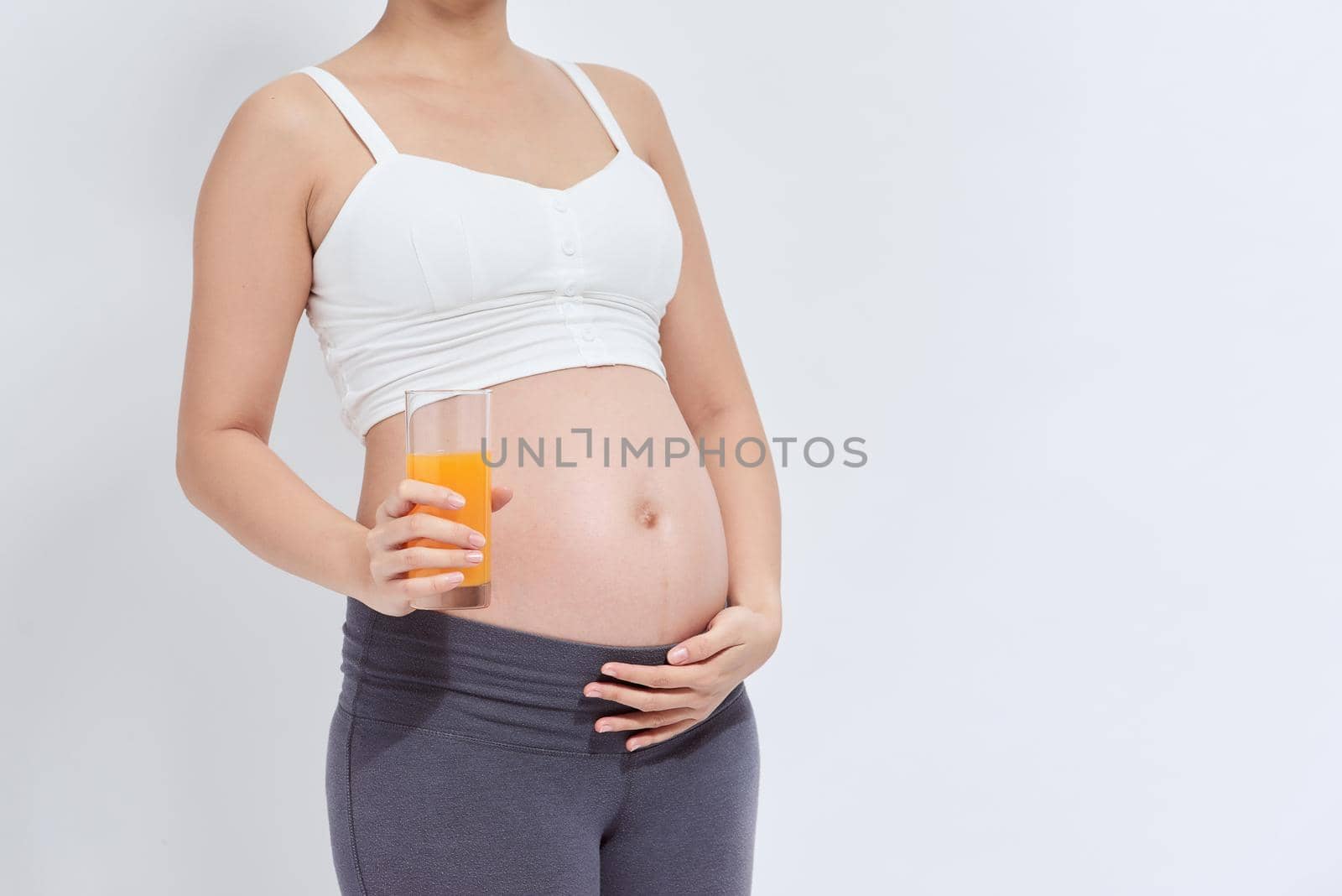 Charming pregnant woman holding a glass of orange juice while standing by makidotvn