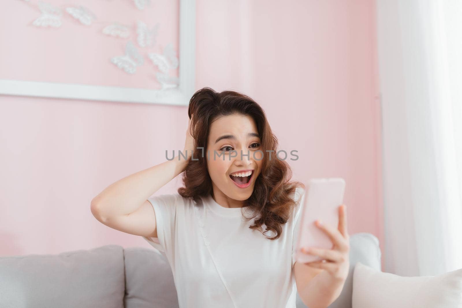 surprised shocked woman looking at phone screen sitting on a sofa in apartment at home by makidotvn