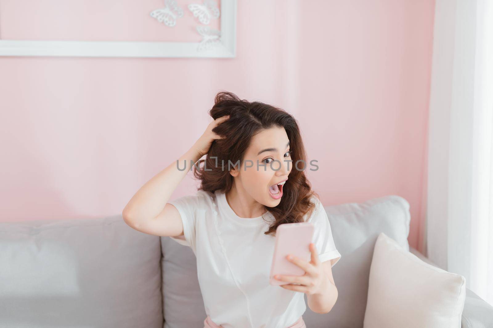 Angry woman screaming on the phone sitting on sofa in bright living room by makidotvn